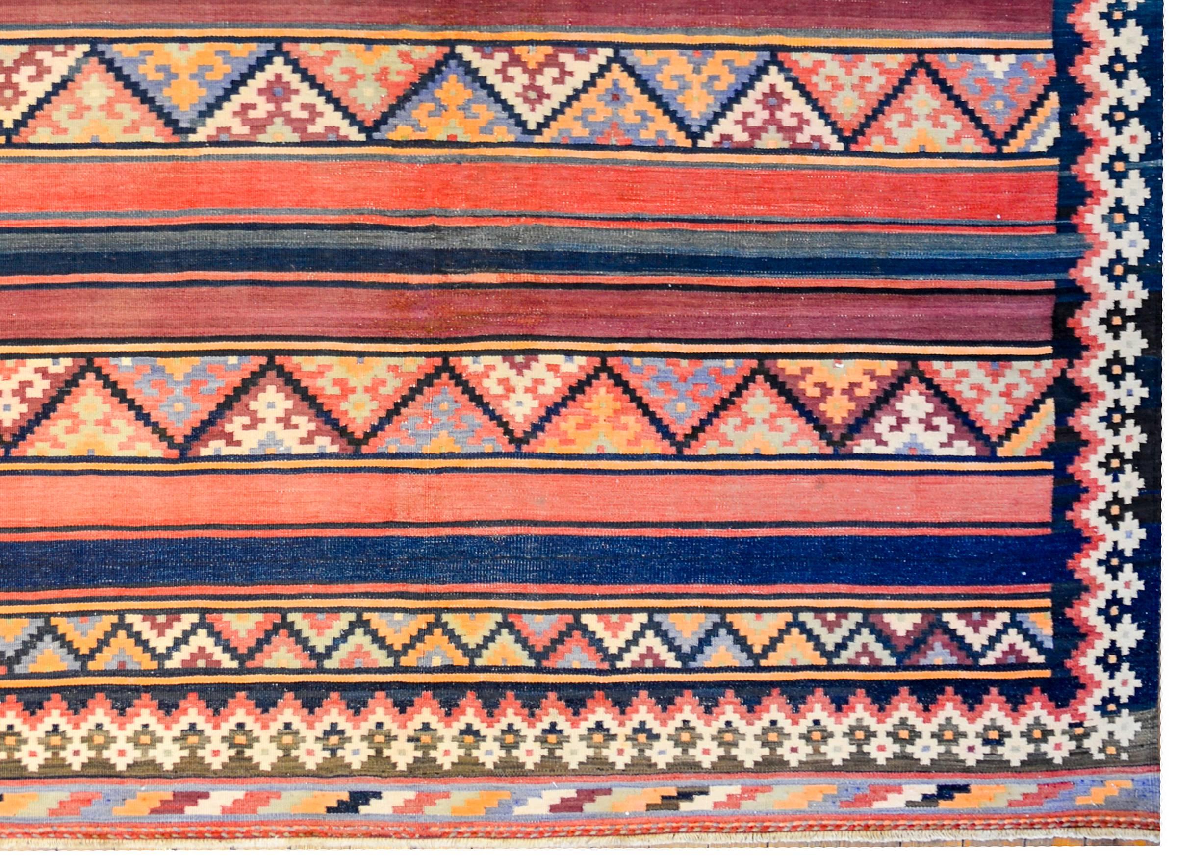 A beautiful early 20th century Persian Zarand Kilim runner with a fantastic pattern of alternating boldly multicolored stripes and stripes with stylized flowers, woven in crimson, indigo, brown, and natural colored wool. The borer is wonderful, and