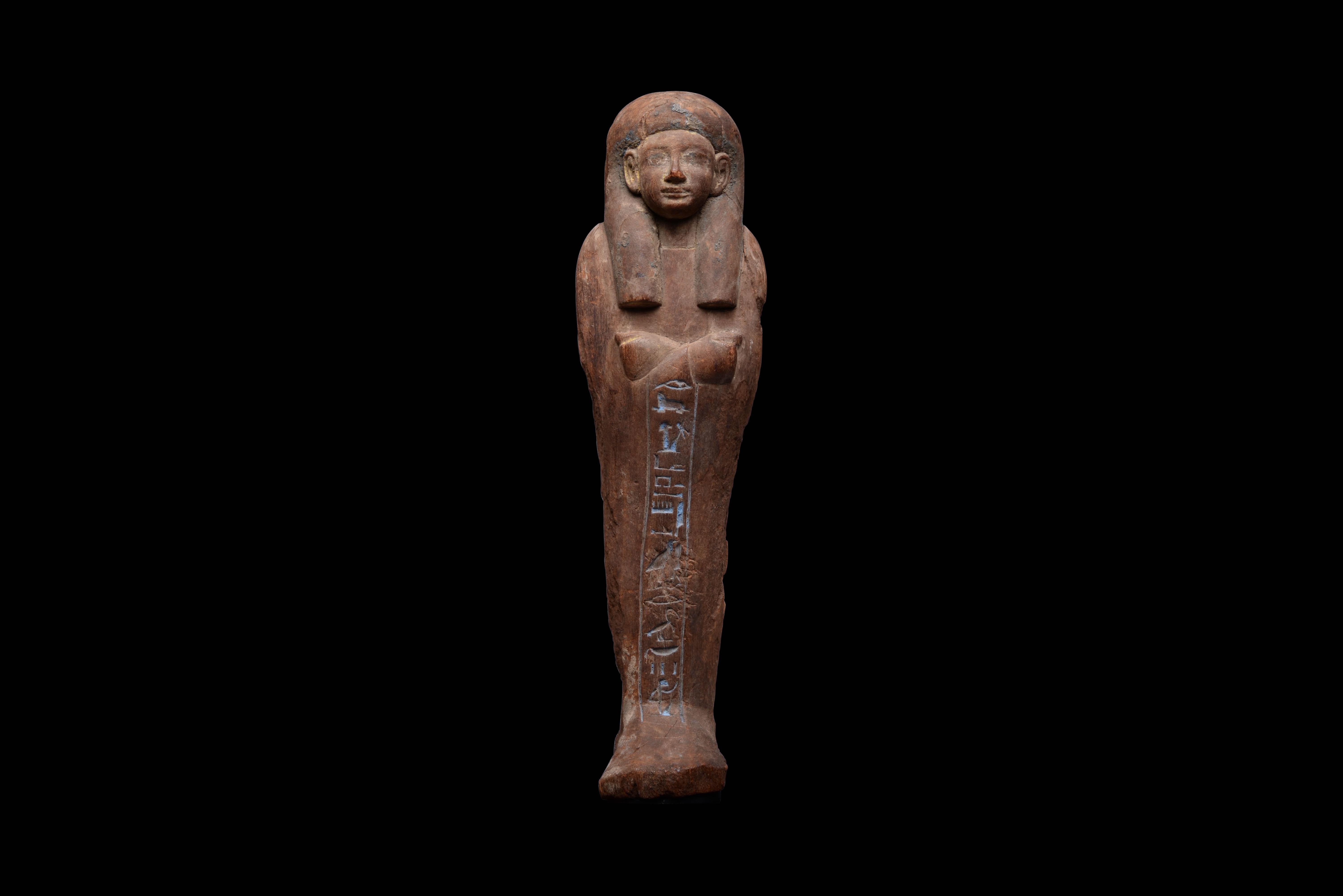 Finely carved in wood with remnants of blue and gold gesso, this beautiful mummiform shabti was deposited in the tomb of Iuferbaku to act as his servant in the afterlife and perform manual labour in his stead. A single frontal column of hieroglyphs,