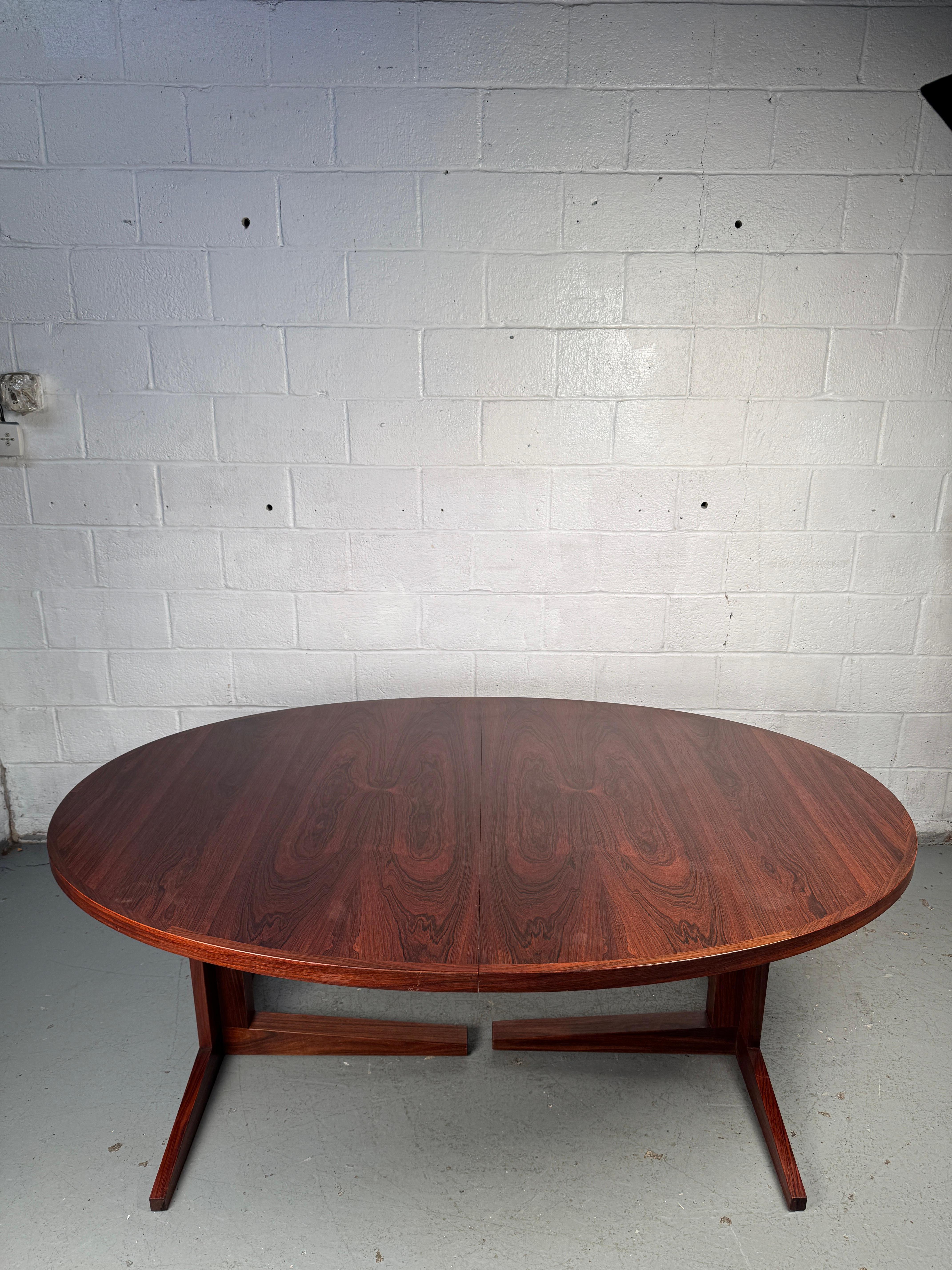 Elégante table de salle à manger moderne du milieu du siècle, fabriquée en bois de rose richement grainé. Conçue avec un profil élégant et une finition chaleureuse, la table s'agrandit avec deux feuilles pour accueillir confortablement les plus