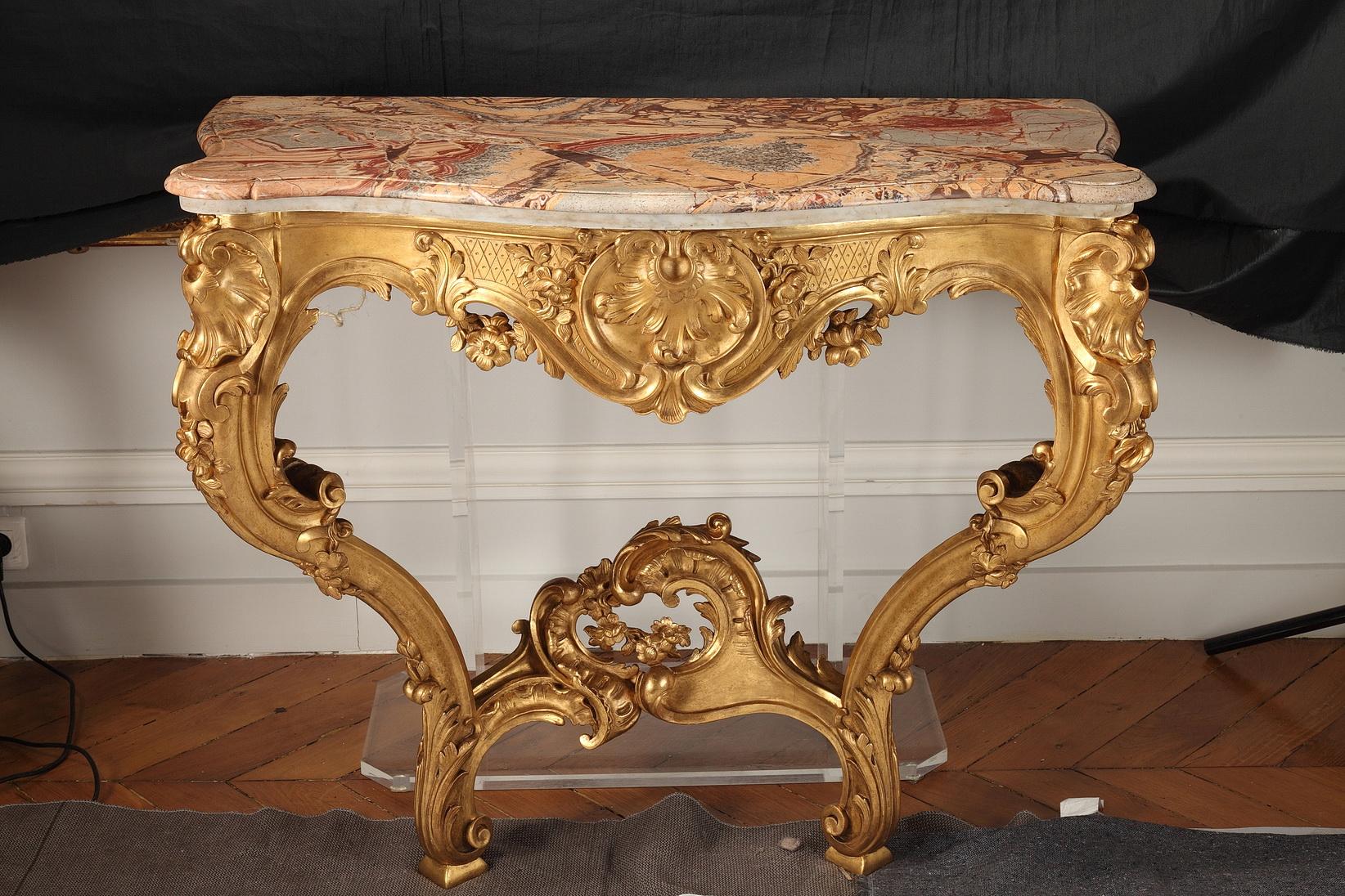 The giltwood console table has a marble top above a large foliated giltwood pattern, reying on two volute legs joined by a stretcher with asymmetrical foliated ornament. The mirror with a rectangular plate bordered by two giltwood mouldings,