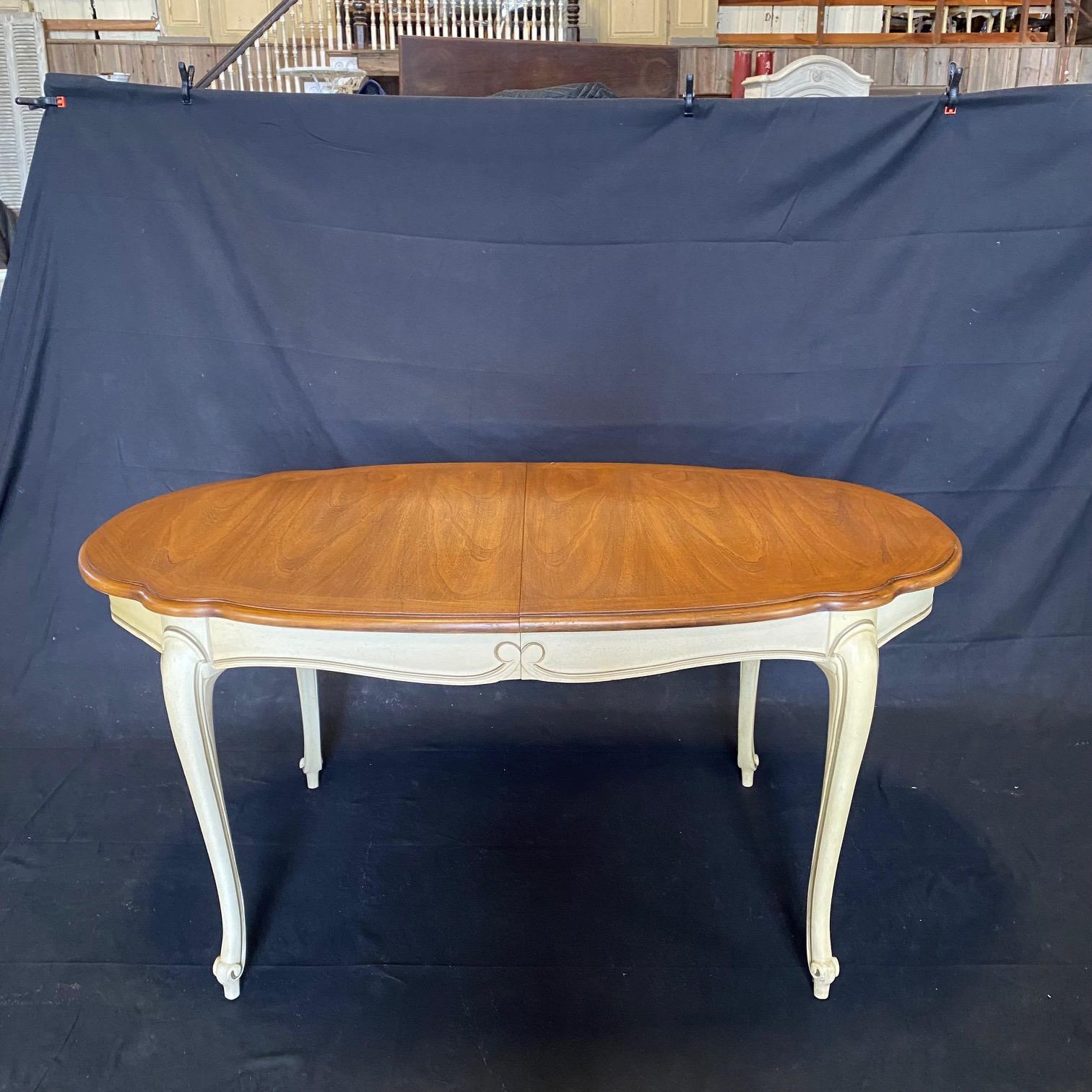 Lovely Louis XV style dining table having gorgeous walnut top with two leaves. The extendable dining table features a wooden top with curved molding details raised on four carved cabriole legs with ivory trim outlines. Open with leaves: 92