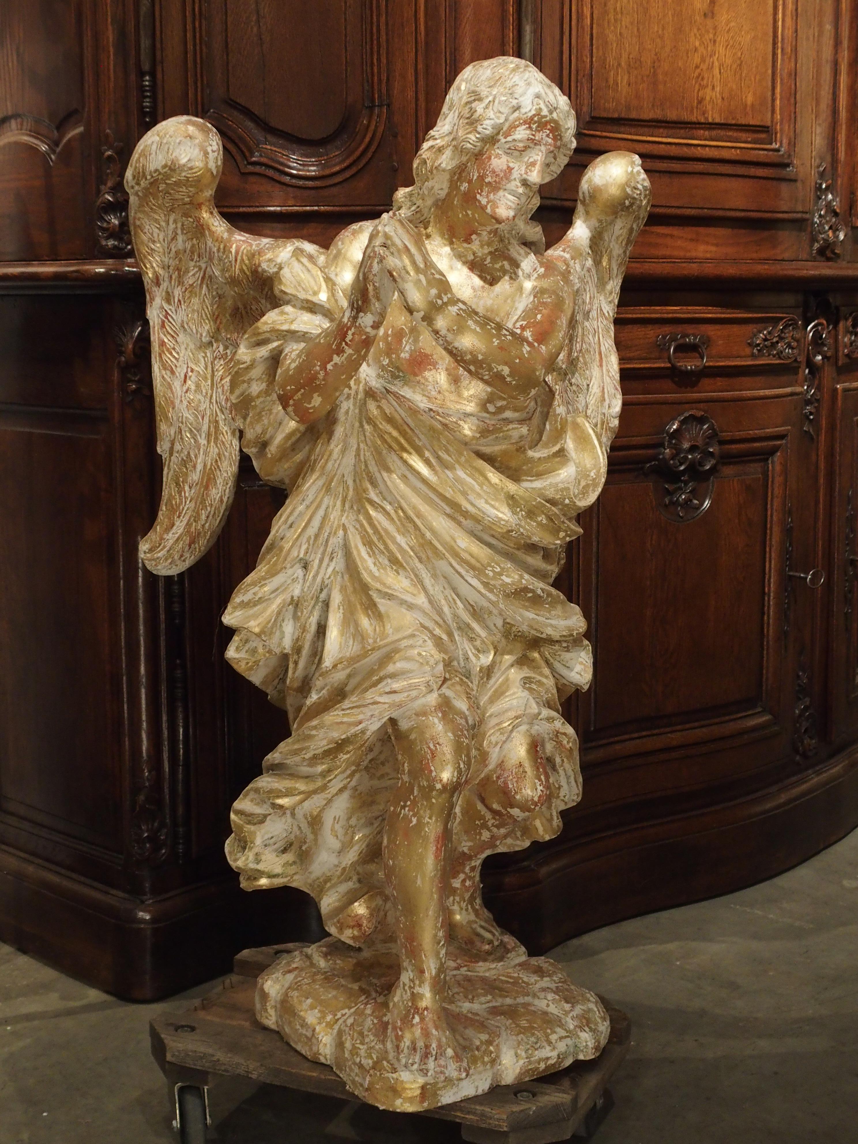 This parcel paint and giltwood statue is over 38 inches high and has been carved from a single piece of wood. It was made in France in the 20th century and has gracefully carved draping and features. With his head tilted to the side and his hands in