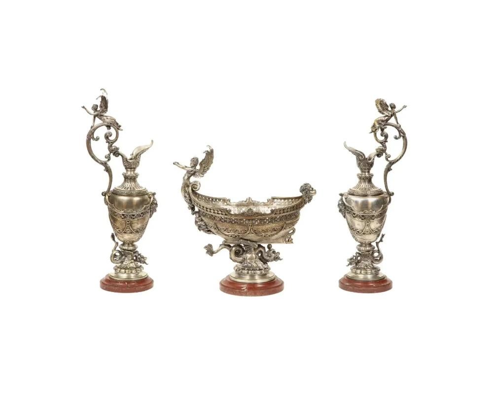 Beautiful French three-piece silvered bronze table garniture, 19th century.

Comprising of a centerpiece / jardinière and a pair of ewers, all on rouge marble bases.

The centerpiece in the form of a nef and figural mounts sitting on a dragon.