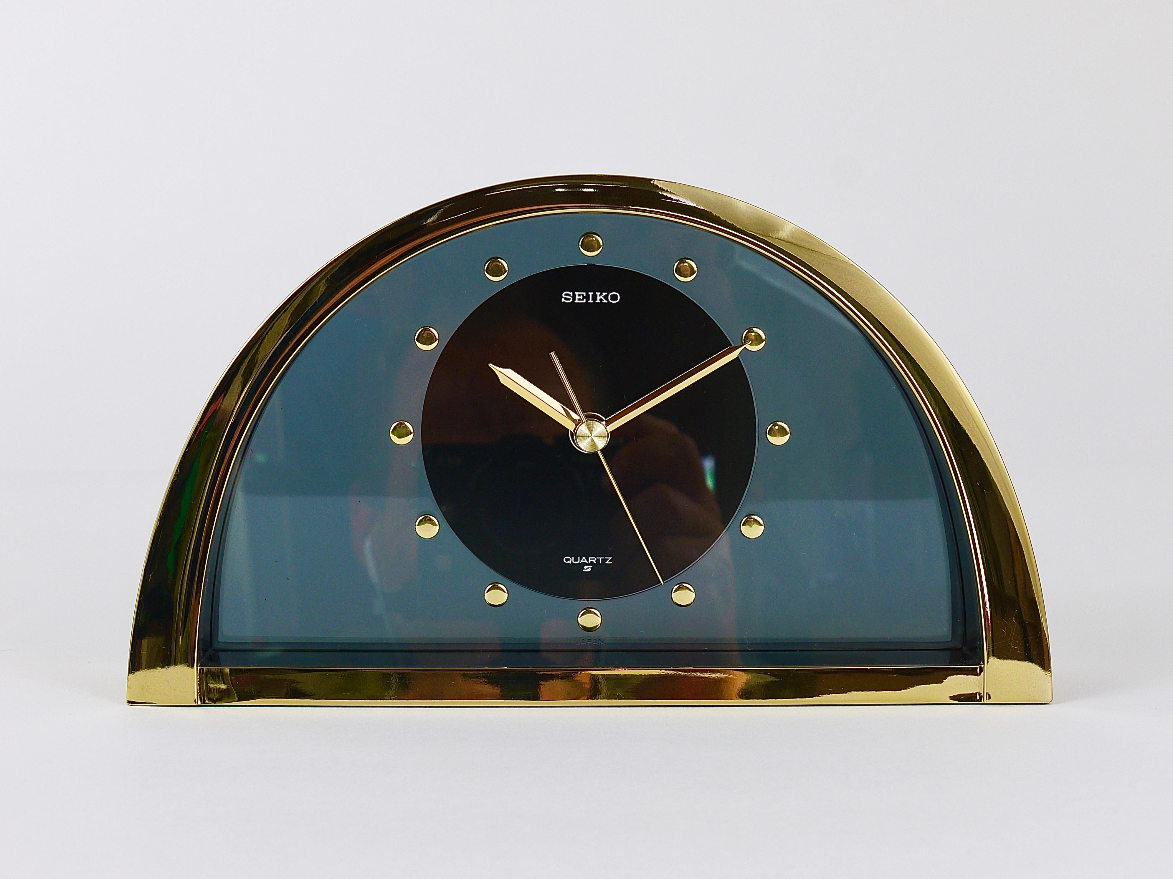 A decorative Hollywood Regency desk or table clock from the 1980s. It has a partly brushed and polished brass housing with nice golden handles and a smoked-grey transparent clocks face. Executed by Seiko, Japan. In excellent condition, a very