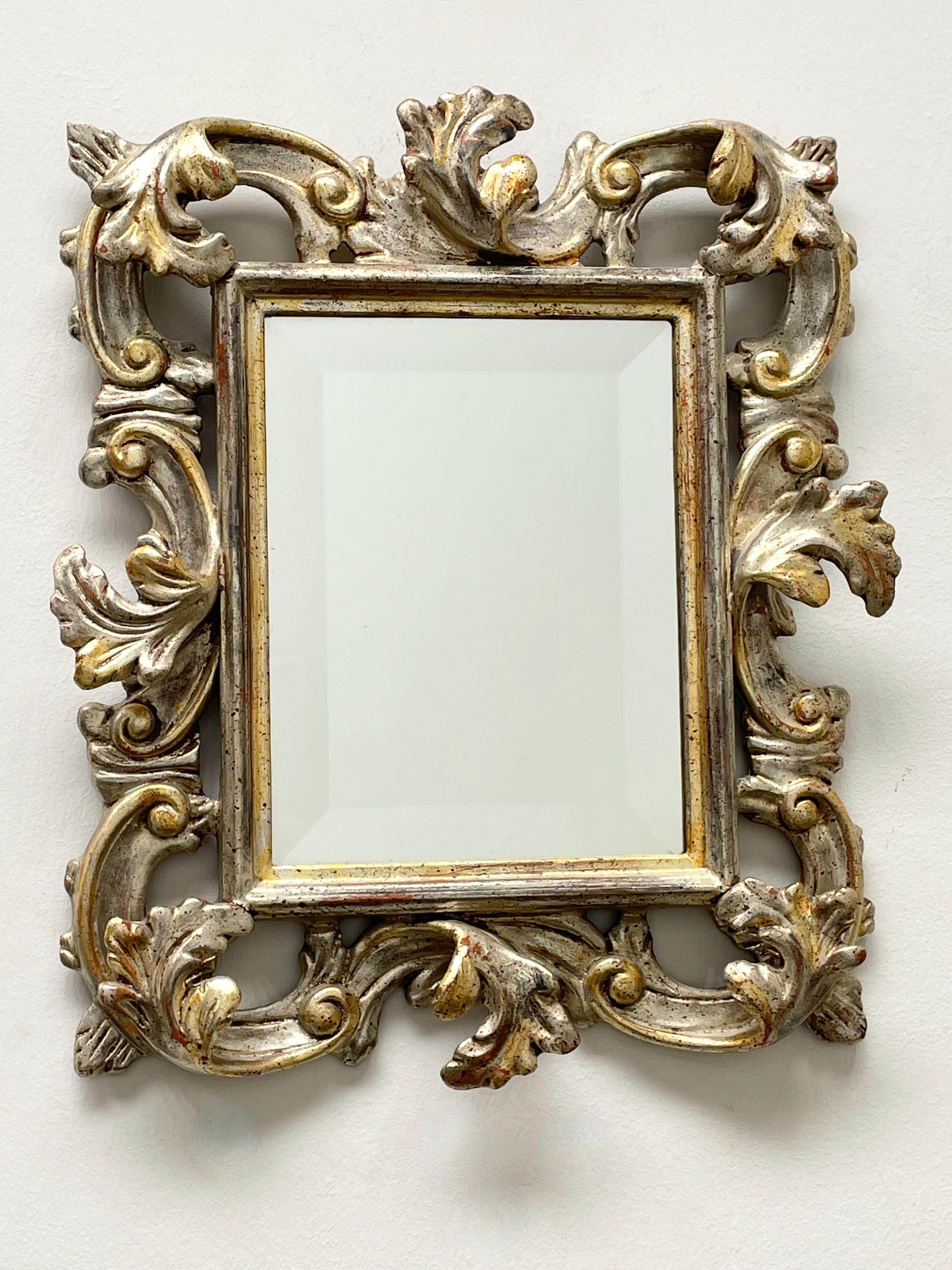Superbe miroir en faïence de style Hollywood Regency. Le cadre en bois sculpté à la main, doré et argenté, entoure un miroir en verre. Le miroir lui-même mesure environ 9 pouces de haut et 7 pouces de large. Fabriqué en Allemagne, dans les années 30