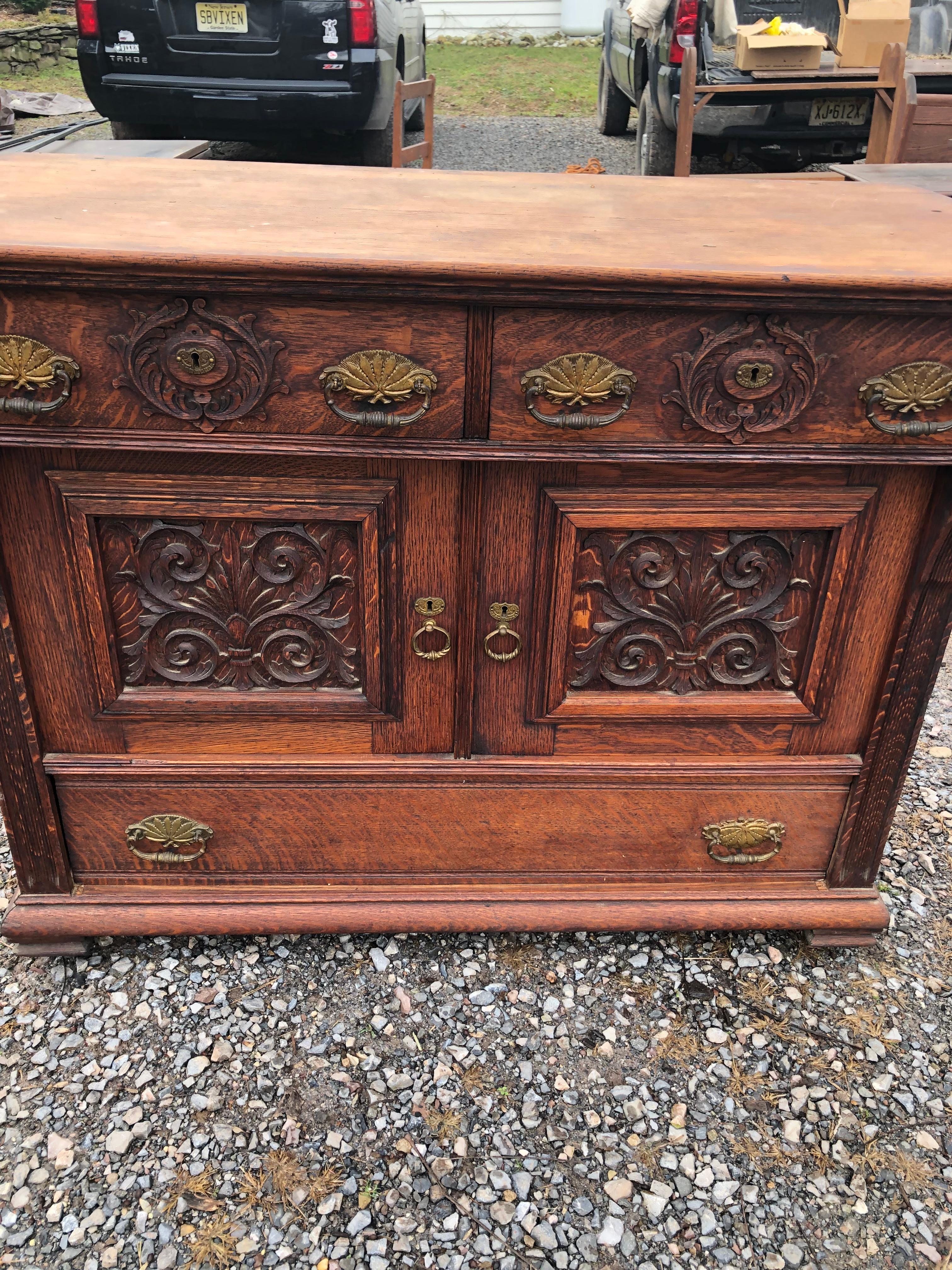 Beautifully carved impressive Victorian oak dresser or sideboard having lots of storage including two top drawers, two paneled doors with interior storage, and one large bottom drawer.  Incredibly handsome brass hardware.