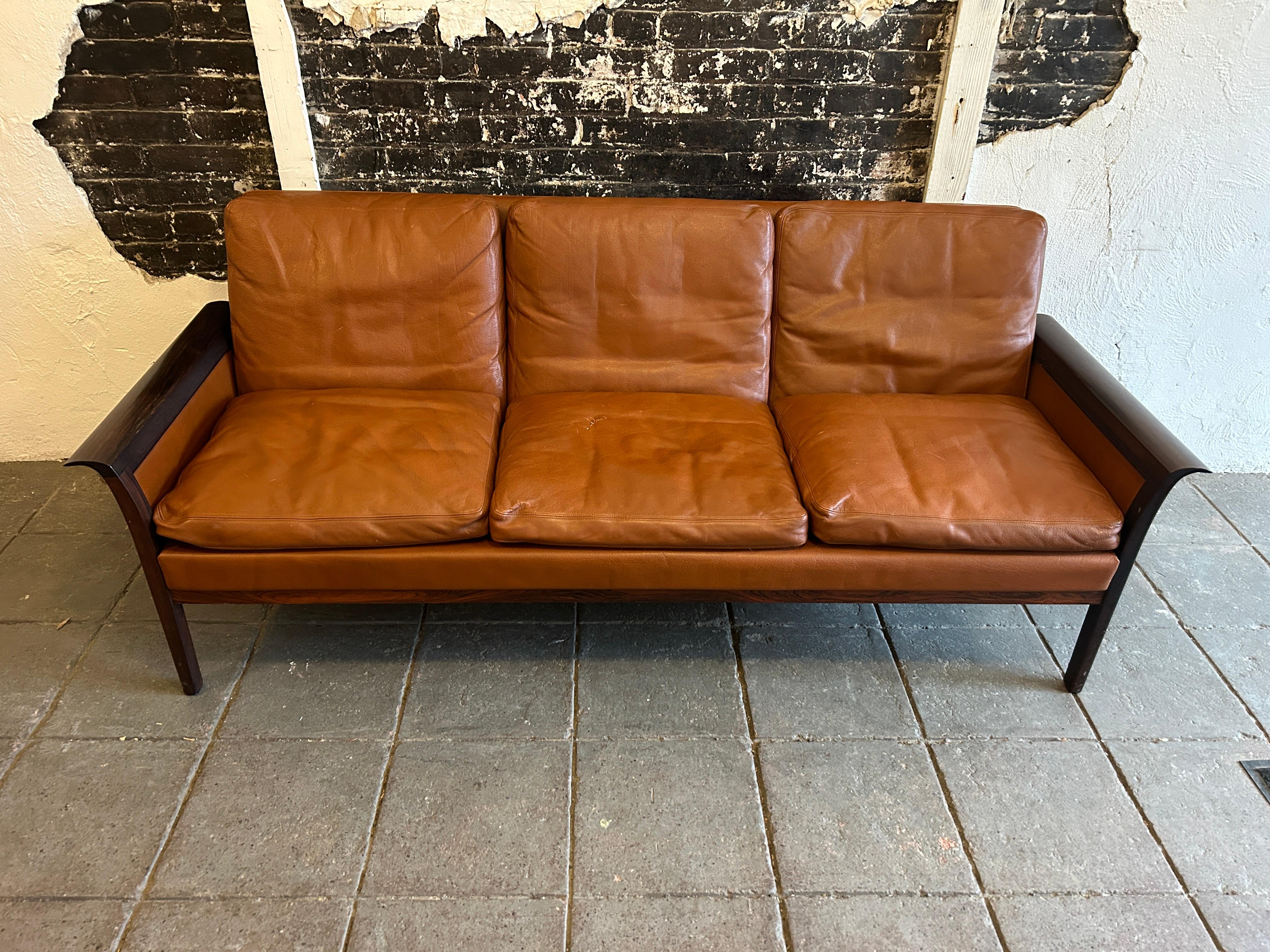 Beautiful Knut Saeter for Vatne Mobler Tan leather and rosewood three-seat sofa couch. All original cognac brown leather upholstery worn in nicely. Stunning rosewood curved arms and legs. Very solid 3 seat cognac leather sofa with original down