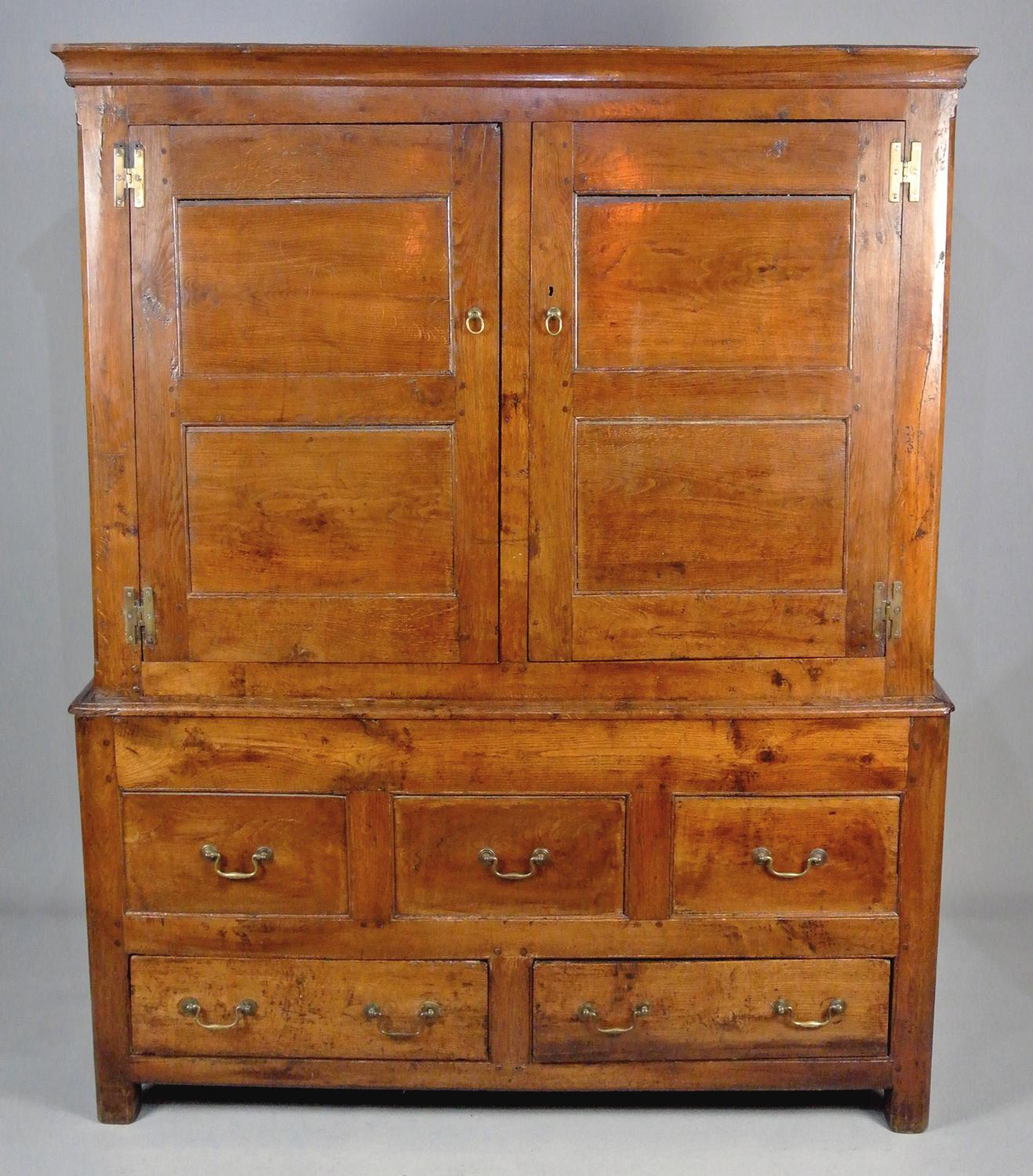 With a fantastic colour and in excellent original condition this large English oak, yew wood and fruitwood press cupboard was made by skilled hands in around 1680.

The two substantial doors with double fielded panels open on solid brass H hinges to