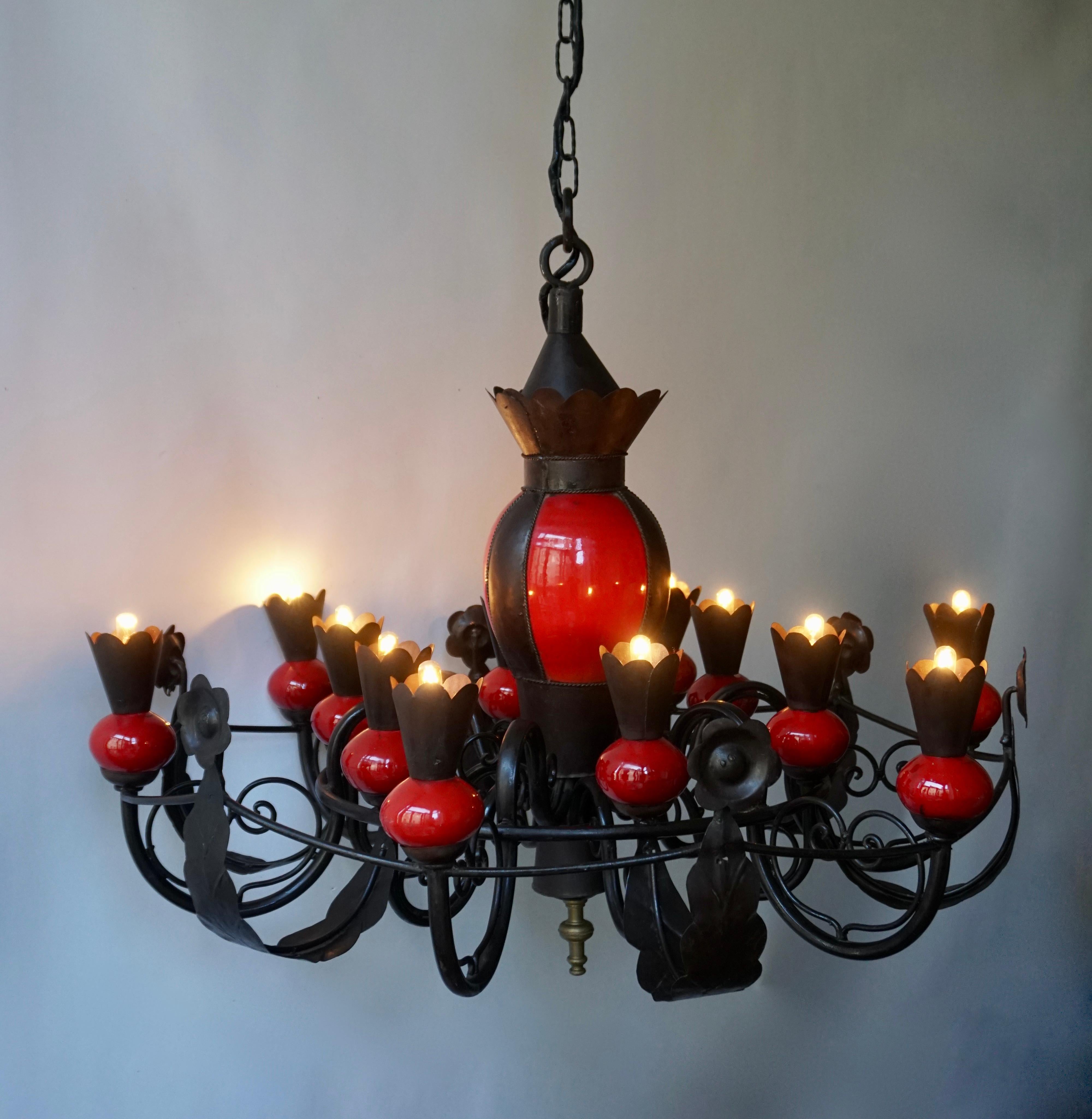 A stunning and grand scale French mid-20th century patinated wrought iron and red ceramic 12-light chandelier.

The light requires twelve single E14 screw fit lightbulbs (60Watt max.) LED compatible.

Measures: Diameter 94 cm.
Height fixture 74