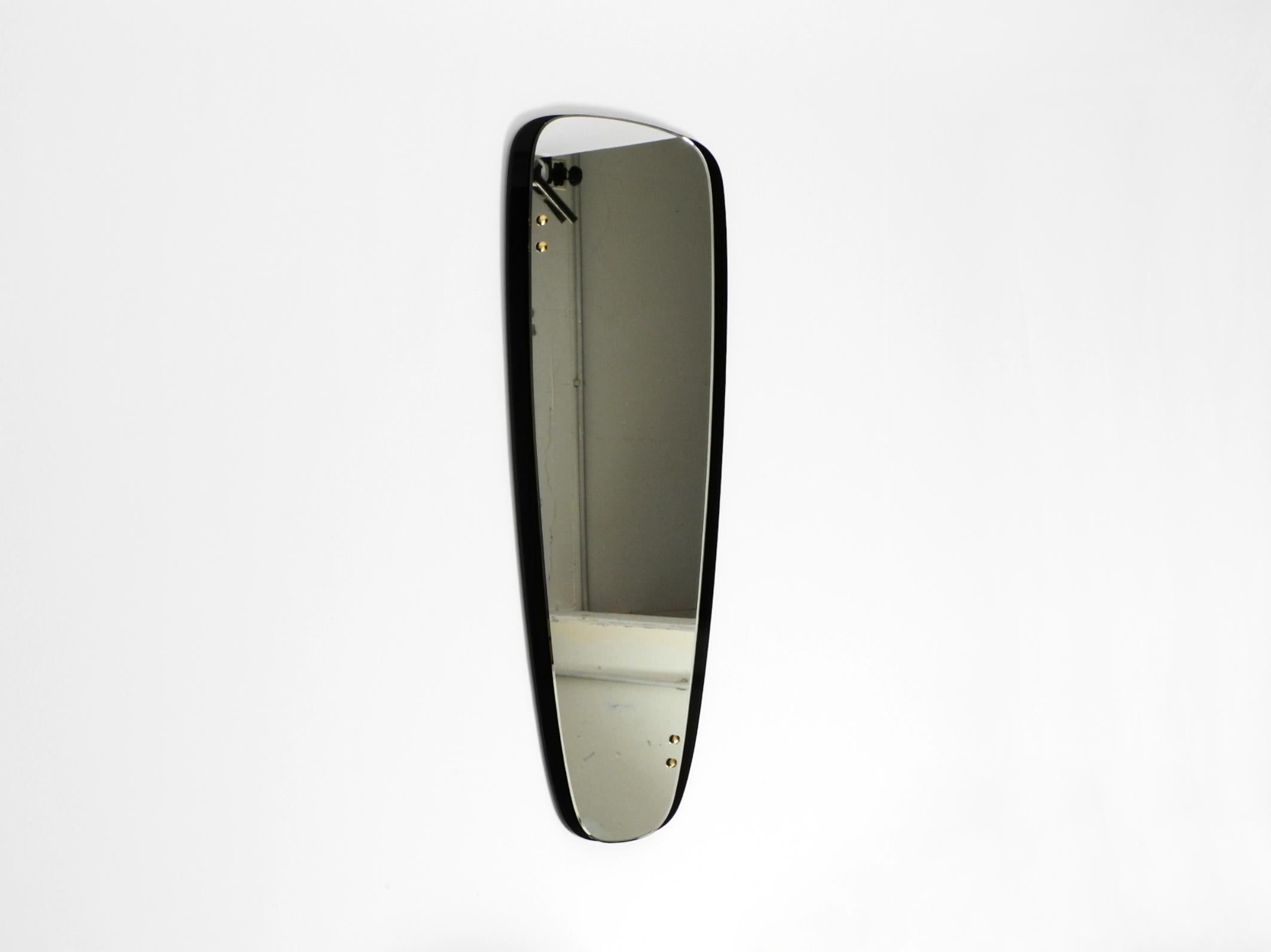 Schöner, hochwertiger, großer Mid-Century Modern Wandspiegel mit Doppelverglasung.
Das Spiegelglas ist auf den schweren schwarzen Glasuntergrund geklebt.
Oben und unten befinden sich zwei große Messingschrauben als Stütze und dekoratives