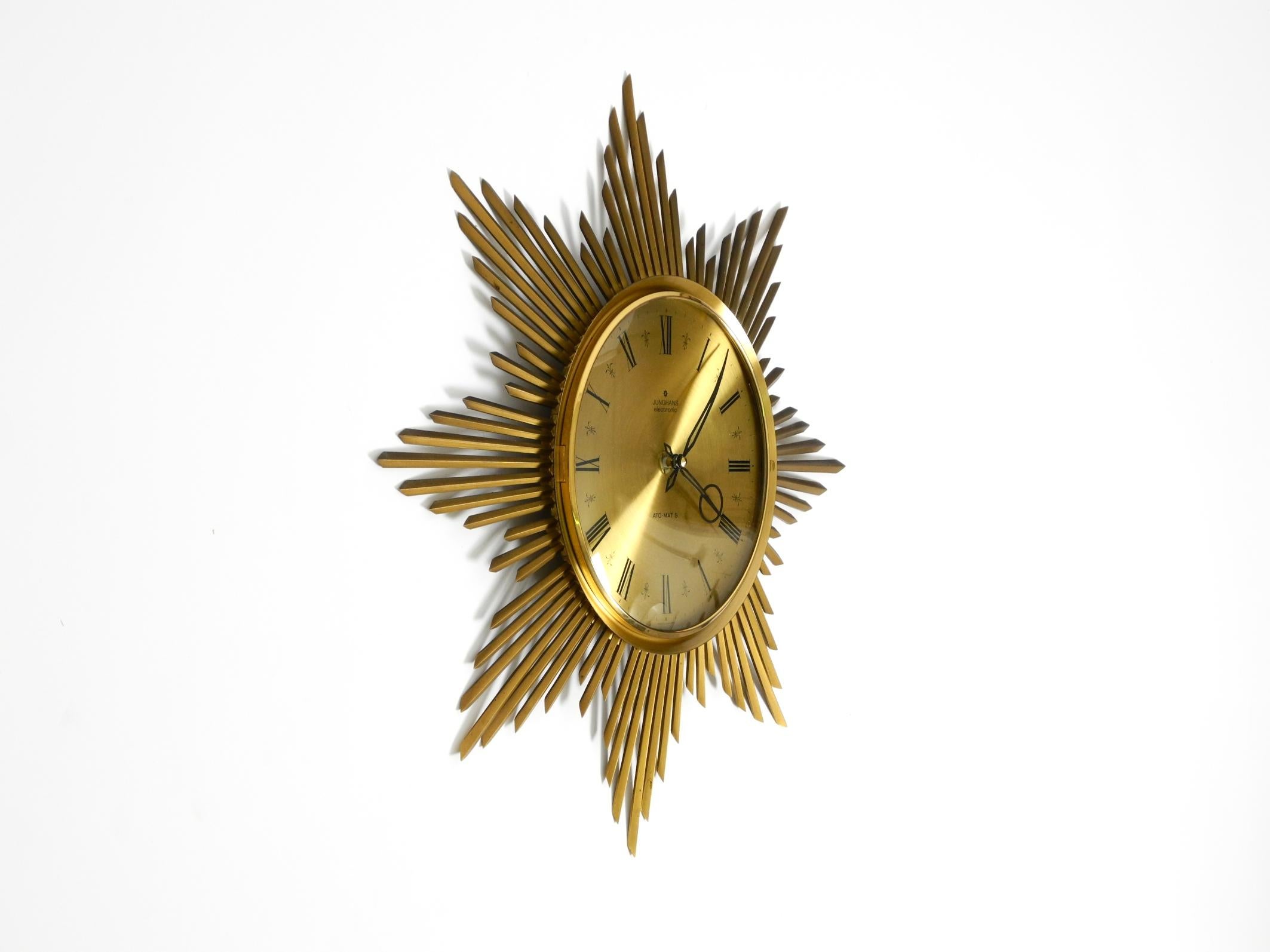 Beautiful, large, original 1960s brass sunburst wall clock by Junghans ATO-MAT.
Very beautiful, elaborate mid-century design. Battery-operated with a new clock mechanism.
Dial with Roman numerals and original minute and hour indicators.
The dial has