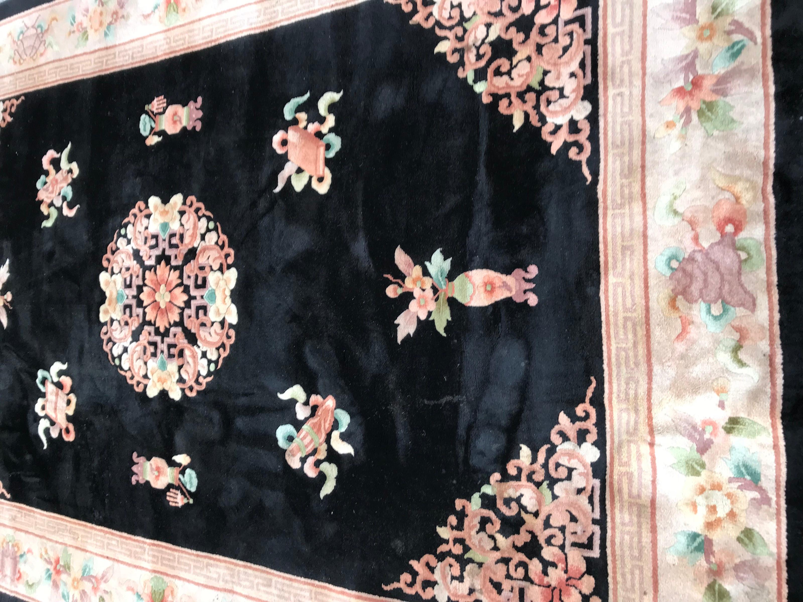 Exquisite late 20th-century Chinese rug featuring a stunning design in vibrant colors. This large rug boasts a captivating Chinese motif on a black field, complemented by floral patterns in pink, green, yellow, and orange. The white field border is