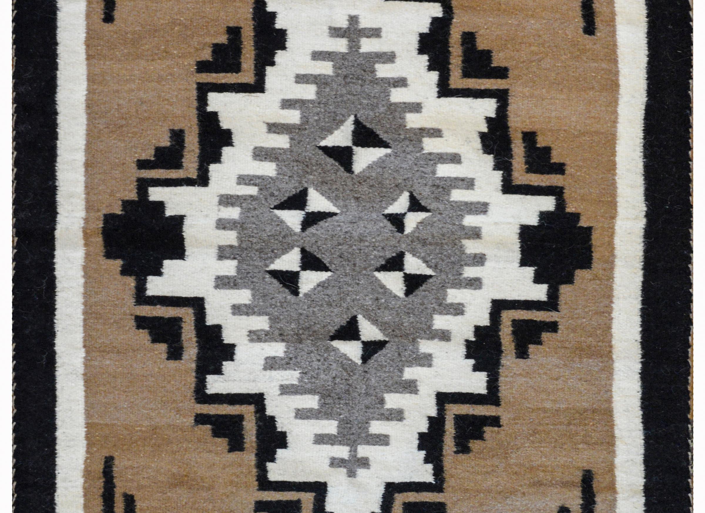 A beautiful mid-20th century Navajo rug with a large central gray diamond with multiple smaller black and white diamonds, and surrounded by geometric patterned white and black diamonds, all on a camel colored ground. The borders are simple solid