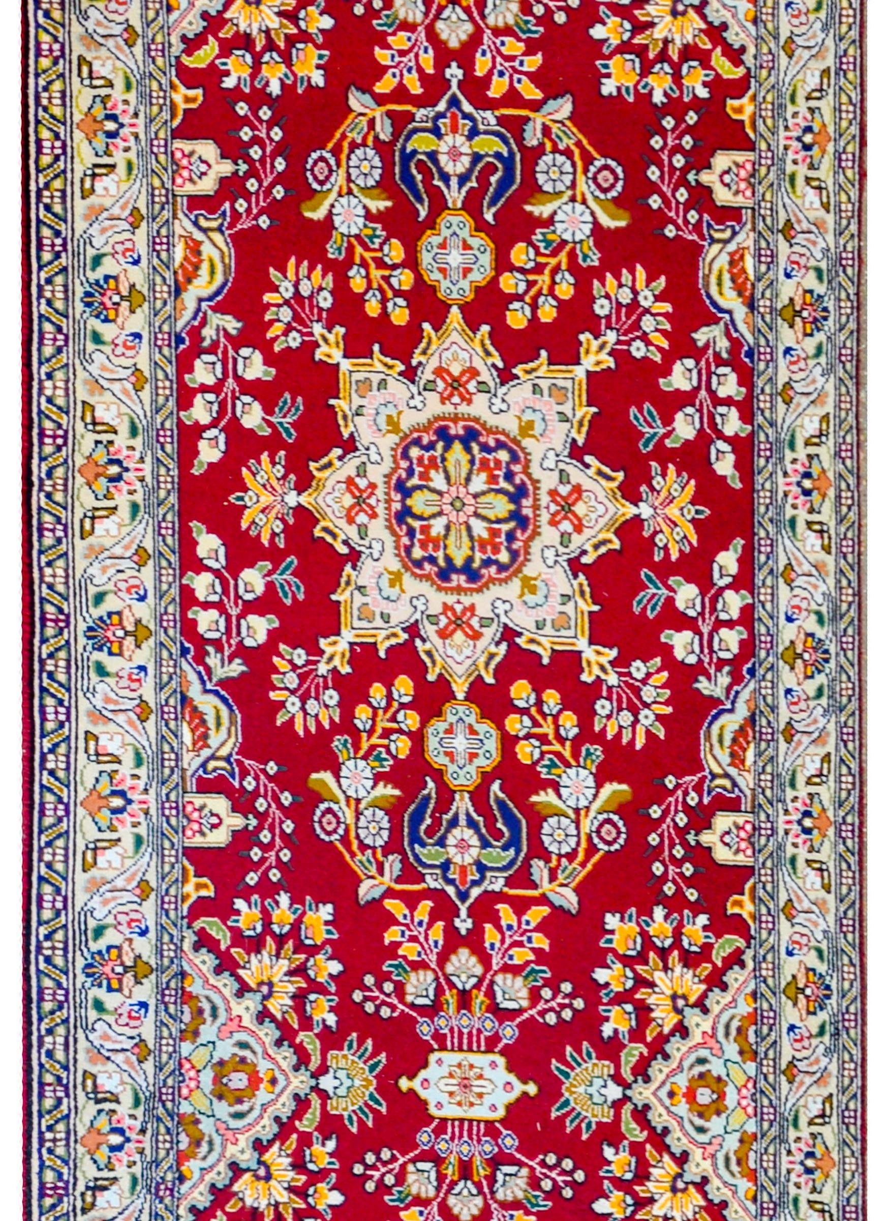 A beautiful mid-20th century Persian Tabriz runner with several large-scale medallions woven in indigo, gold, green, pink and cream colored wool amidst a field of myriad flowers, on a crimson background. The border is sweet with a petite-scales