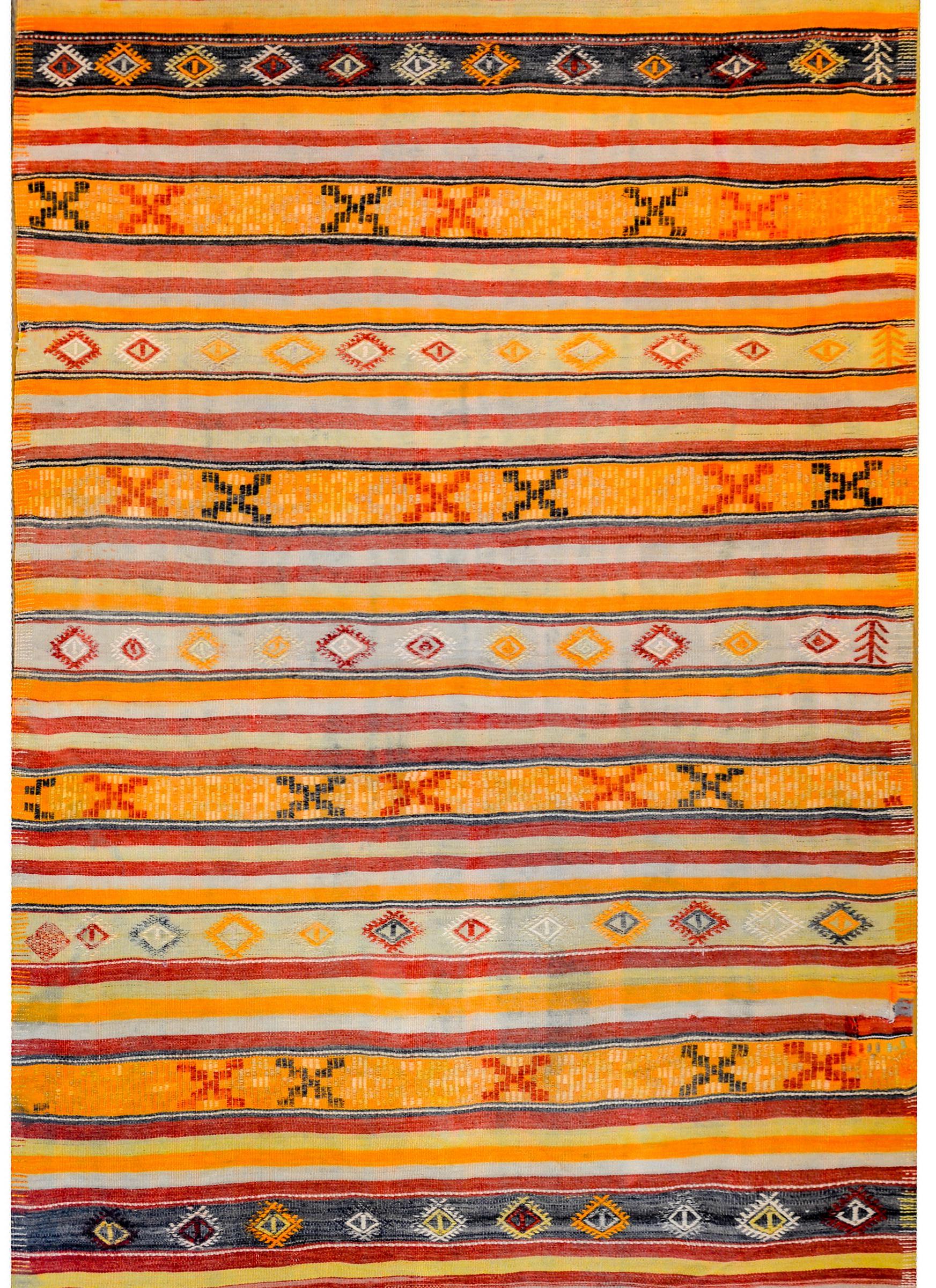 A beautiful mid-20th century Turkish Anatolian Kilim rug with myriad multicolored and geometric patterned stripes woven in black, crimson, orange, cream, and green vegetable dyed wool.