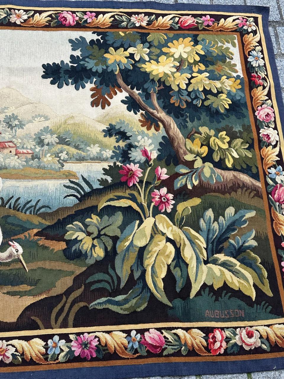 Discover the timeless elegance of this early 20th-century French Aubusson tapestry featuring a captivating design of a bird in the garden.
This tapestry depicts a pastoral landscape in a classical, idyllic style. In the foreground, a white heron or