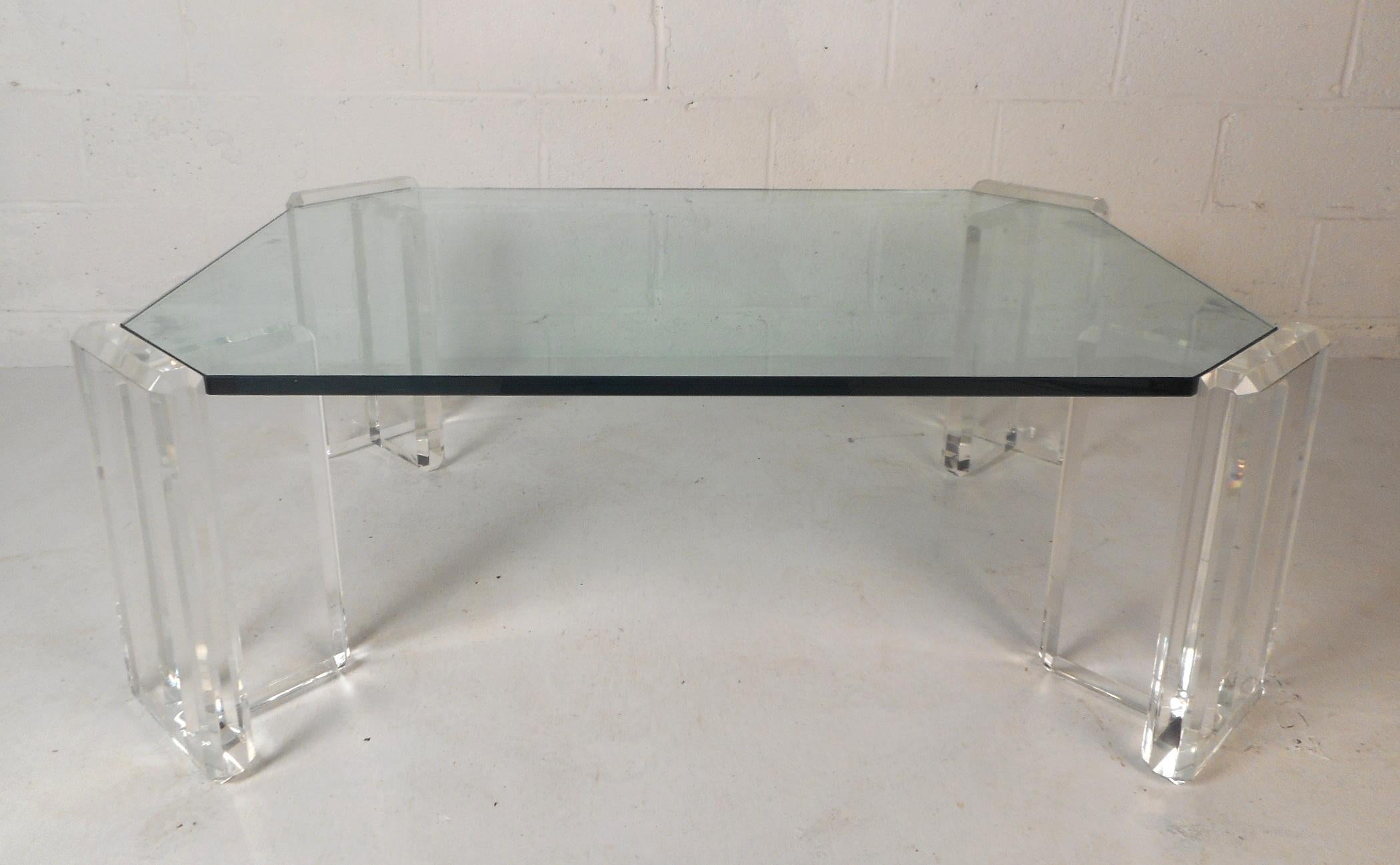 This gorgeous vintage modern coffee table features four individual Lucite bases holding up an extremely thick glass top with bevelled edges. The thick Lucite legs with smooth edges compliment the large glass top making this table an impressive
