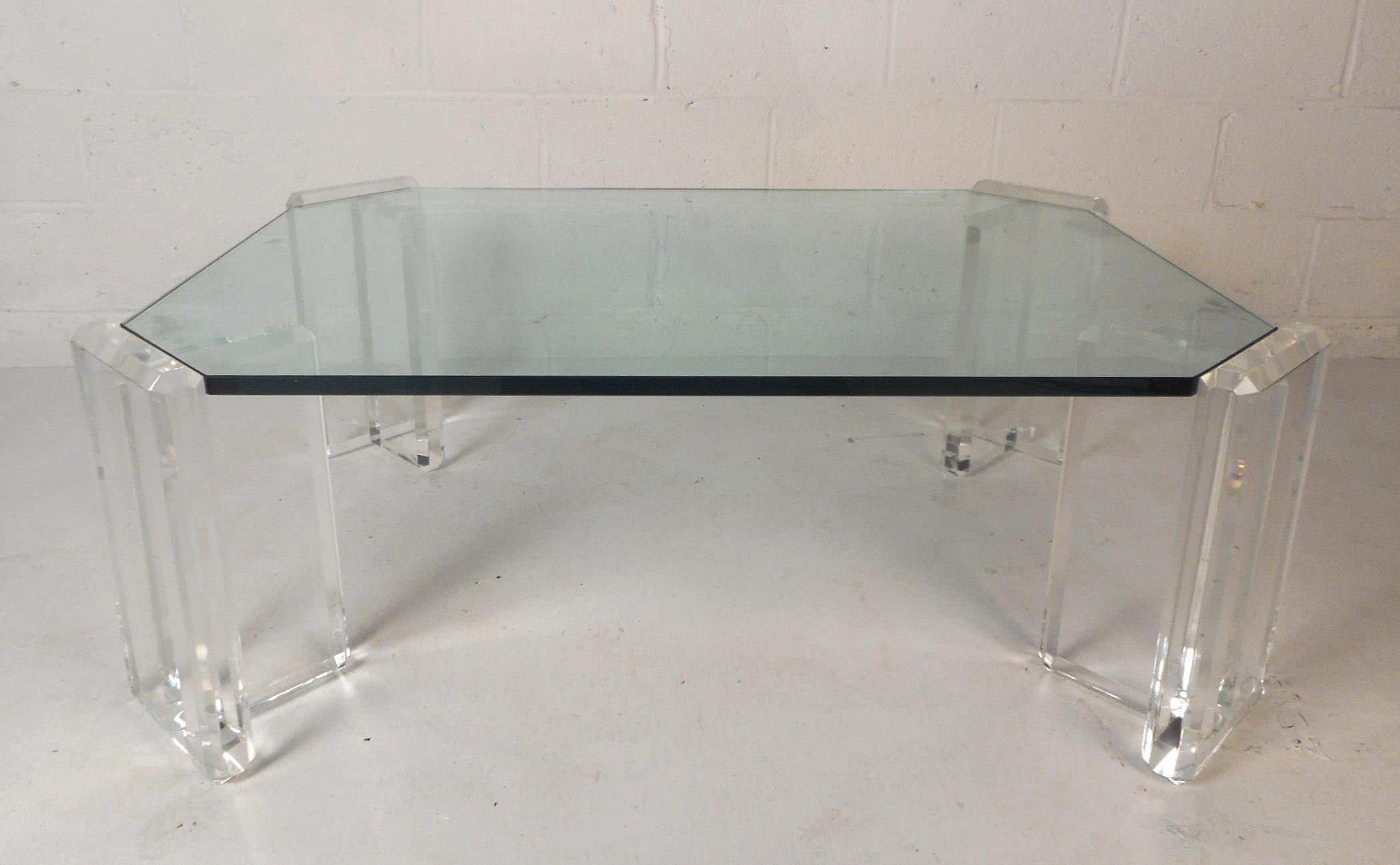 Cette magnifique table basse vintage moderne est dotée de quatre bases individuelles en Lucite qui soutiennent un plateau en verre extrêmement épais aux bords biseautés. Les pieds épais en Lucite aux bords lisses complètent le grand plateau en
