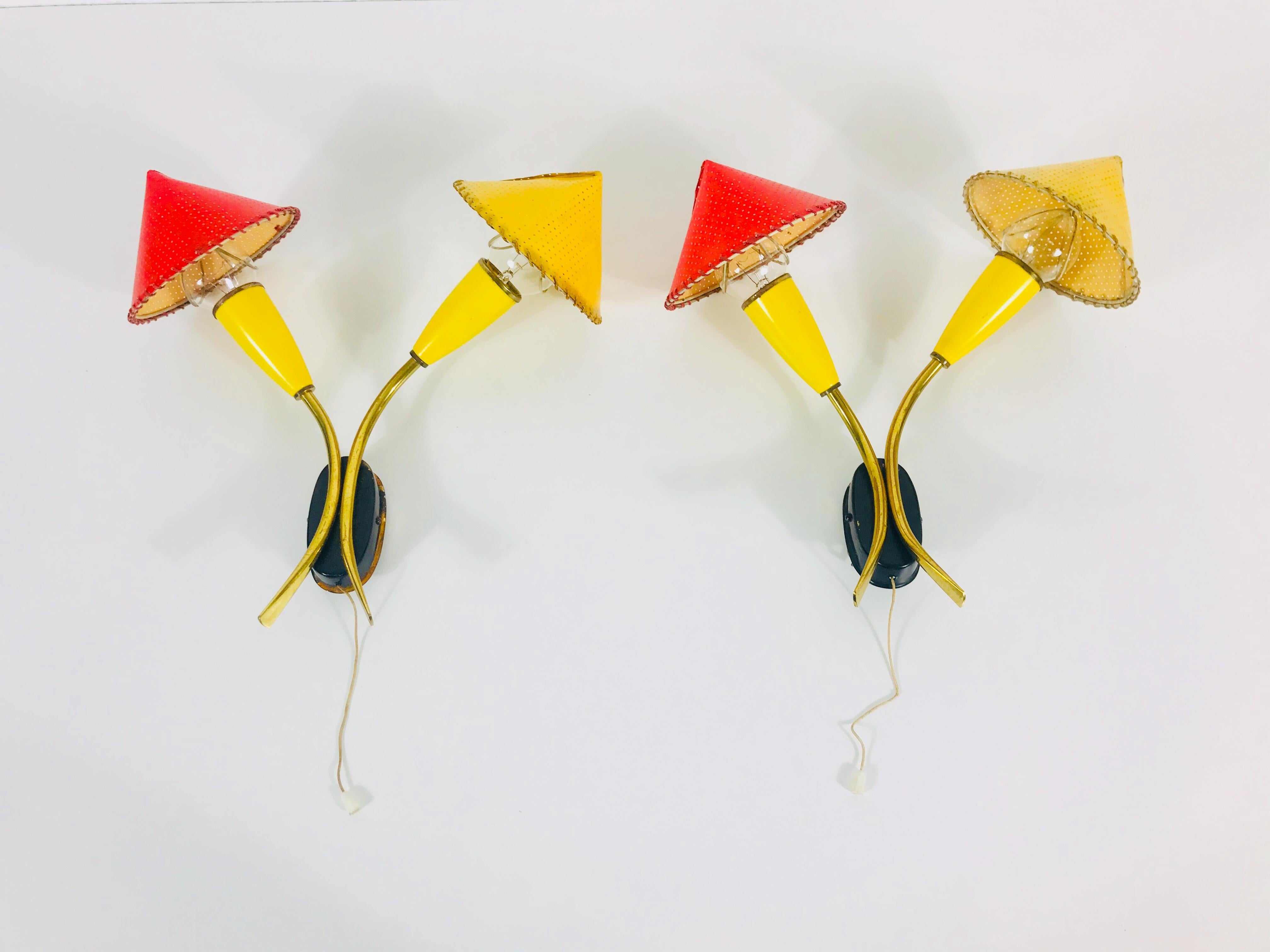 A pair of beautiful Mid-Century Modern wall lamps made in Germany in the 1960s. They can perfectly be mounted on the wall. The body of the lights is made of brass and metal. The fixtures have red and yellow hats which are stuck onto the light