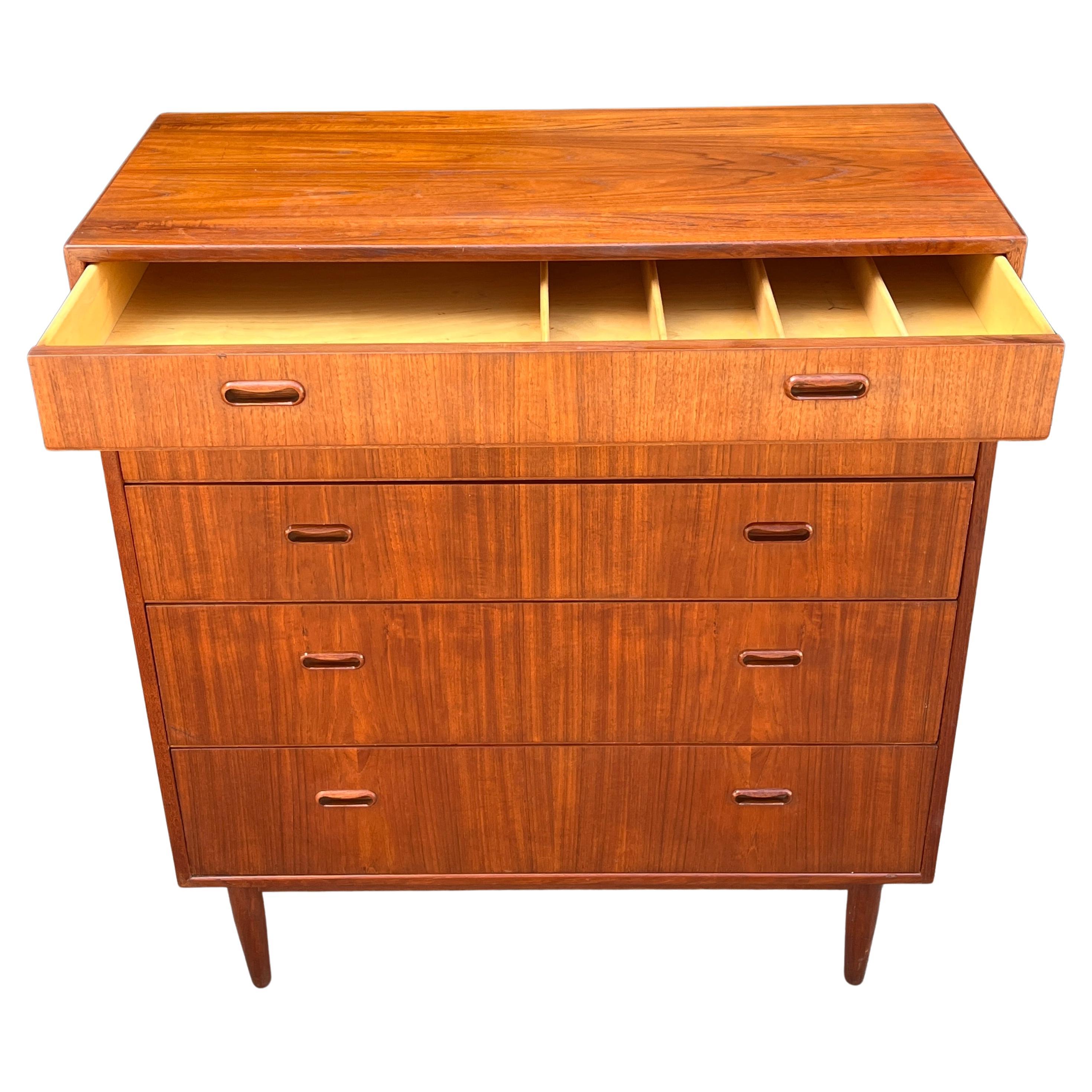 Wonderful teak wood tall boy gentleman's chest featuring 5 drawers total. Having signature oval inset pulls resting on solid teak tapered legs. Showing a warm patina and ready for use.

Still retaining the Maurice Vallecy tag that retailed this unit