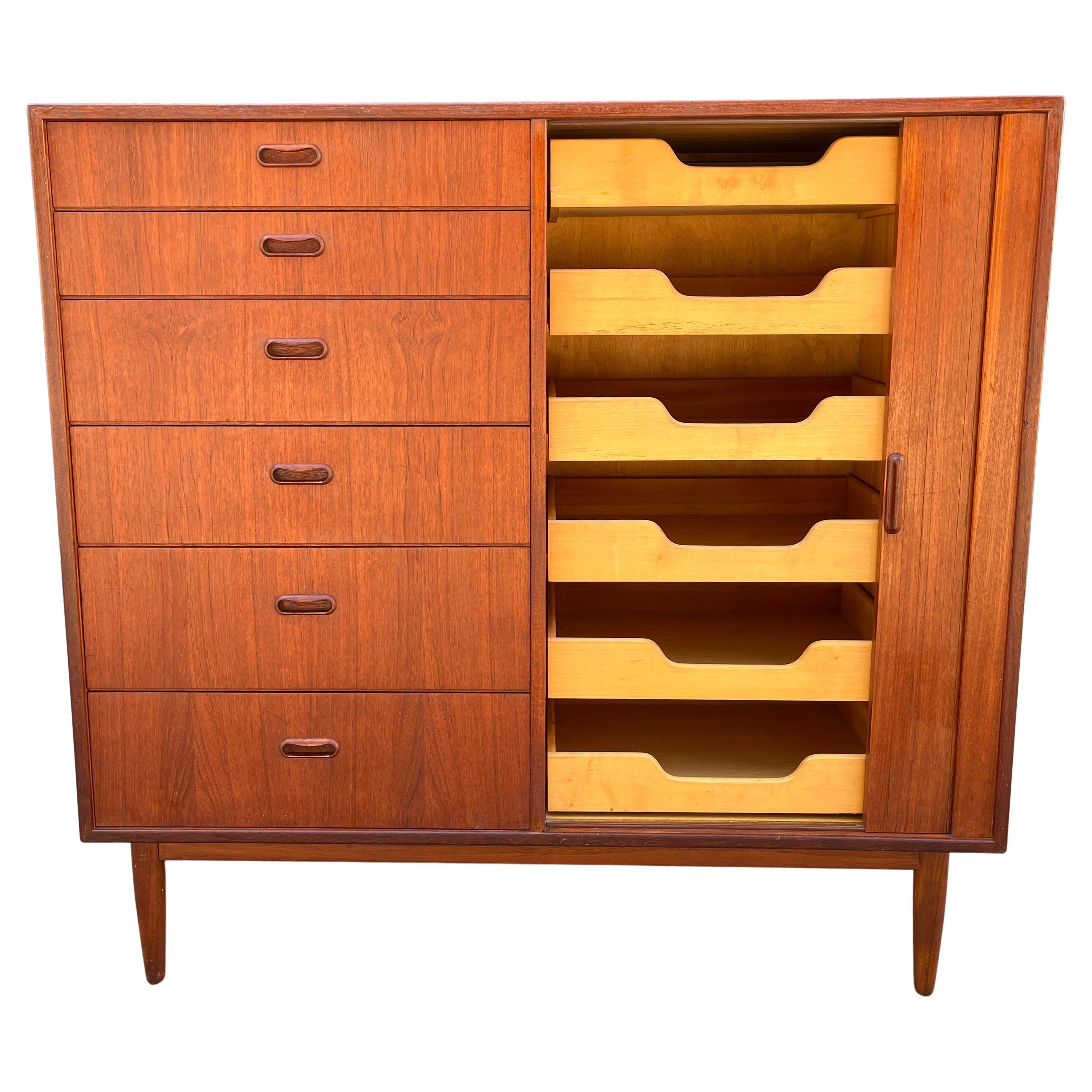 Wonderful teak wood tall boy gentleman's chest featuring 12 drawers total. Left side having signature oval inset pulls and the other half having shallow pull-out drawers concealed behind a tabour door. Resting on tapered solid teak legs. Showing a
