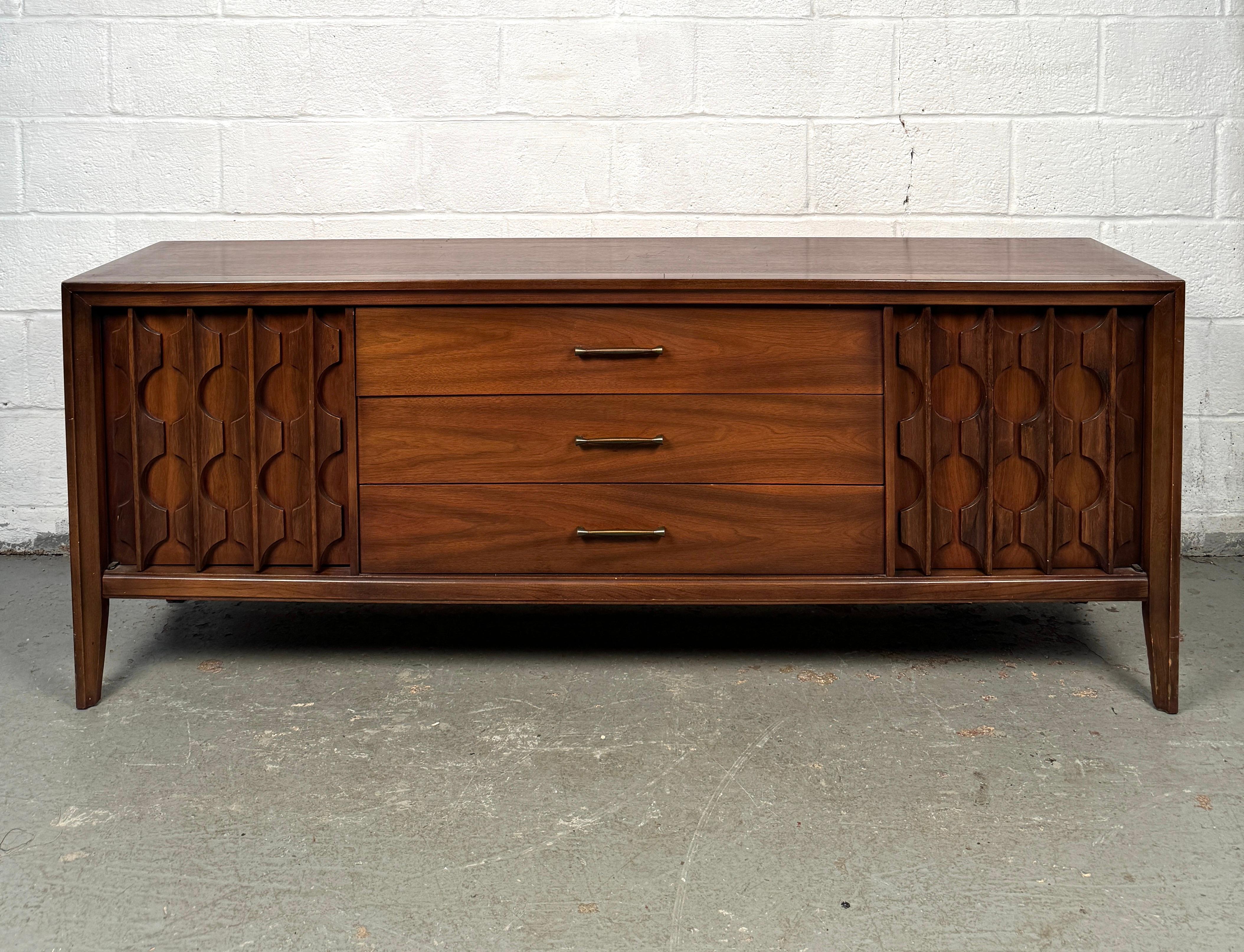 Découvrez l'alliance parfaite de la forme et de la fonction avec cette crédence en noyer du milieu du siècle par Kent Coffey, une pièce sophistiquée qui incarne l'esthétique épurée et intemporelle du design moderne des années 1960. Fabriquée en