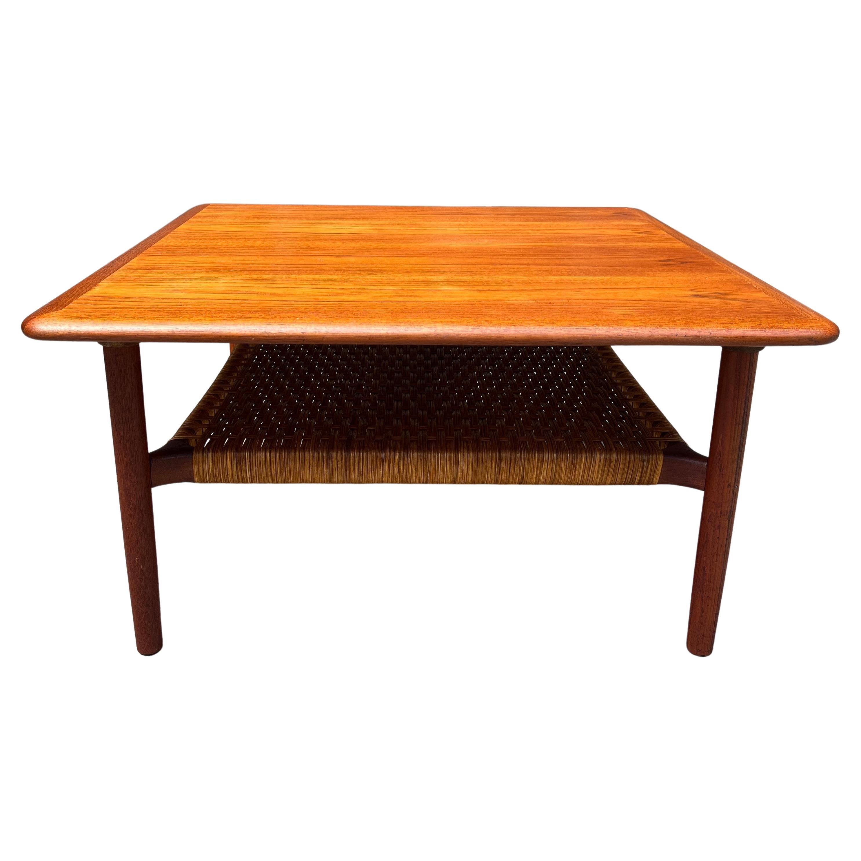 Classic Danish Modern Midcentury coffee table by Gunnar Schwartz. Teak wood with woven cane undershelf. Produced in denmark in the 1950’s. This rectangular table is made out of teak wood and features a woven cane shelf underneath the table top. In