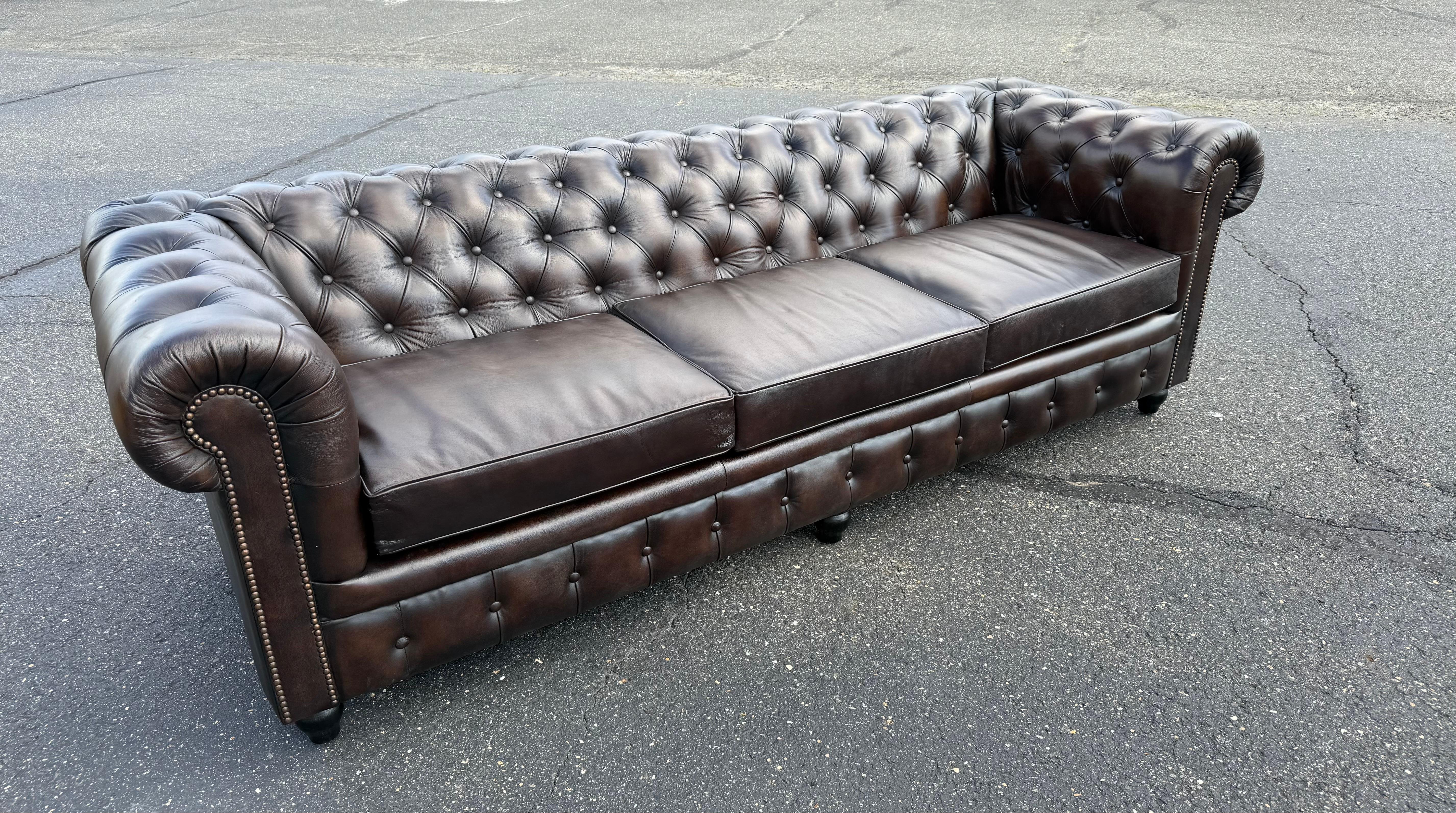 Ce canapé Chesterfield anglais fabriqué sur mesure est revêtu de cuir marron véritable, mettant en valeur la sophistication intemporelle du design britannique traditionnel. Doté d'un dossier et d'accoudoirs profondément boutonnés, d'accoudoirs