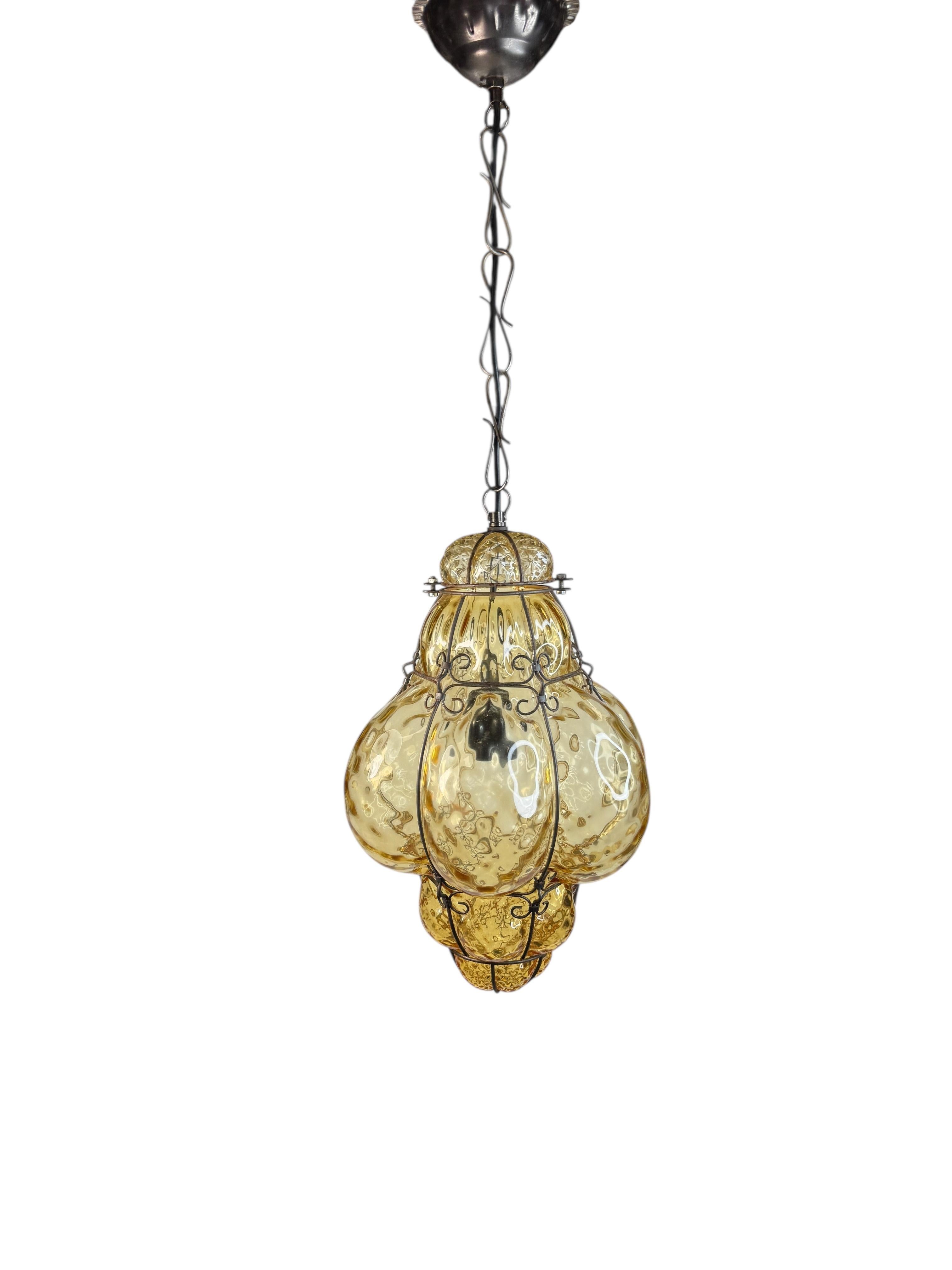 Magnifique lustre en verre de Murano couleur ambre bullé avec cage. Le verre est soufflé à la main avec une teinte ambrée ou fumée et a été créé par un artiste italien sur l'île de Murano dans les années 1960 en Italie.

Cette suspension cage à
