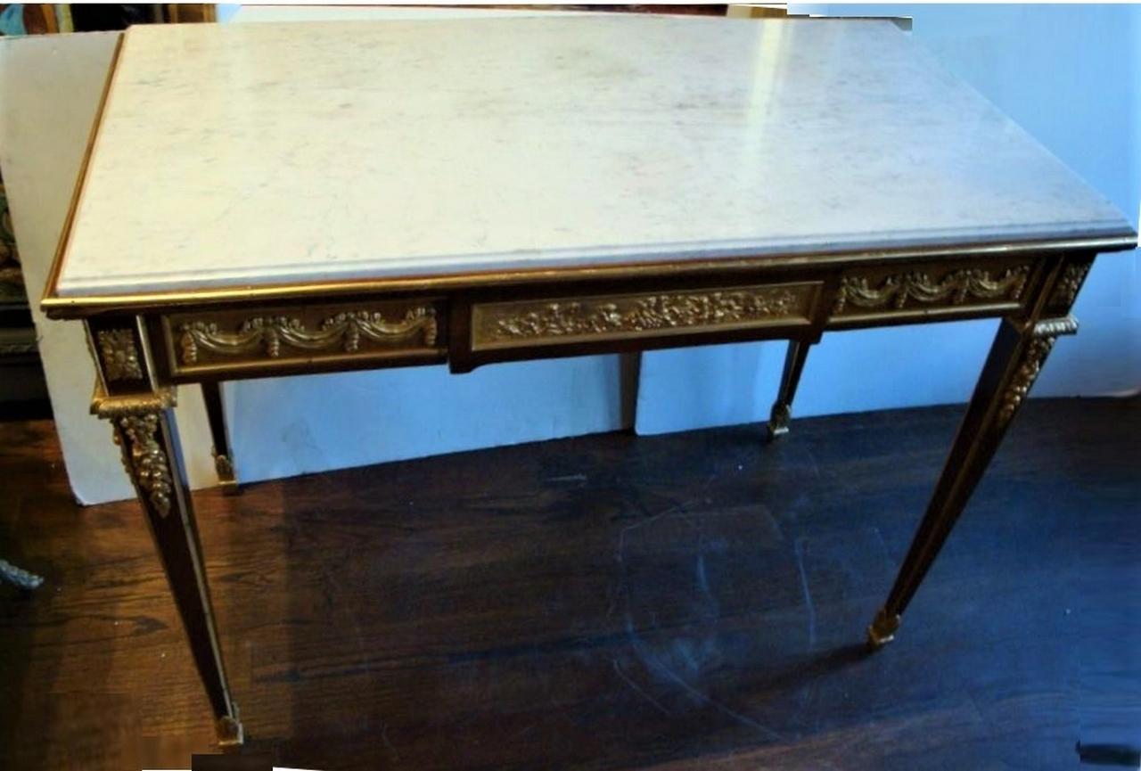 A Beautiful Museum Quality French Ormolu-Mounted Mahagony and Fruitwood Center Table
Circa Early 1900's. The rectangular grey-veined white marble top above a spring-activated frieze drawer centered with cloudborne putti, the angles with rectangular
