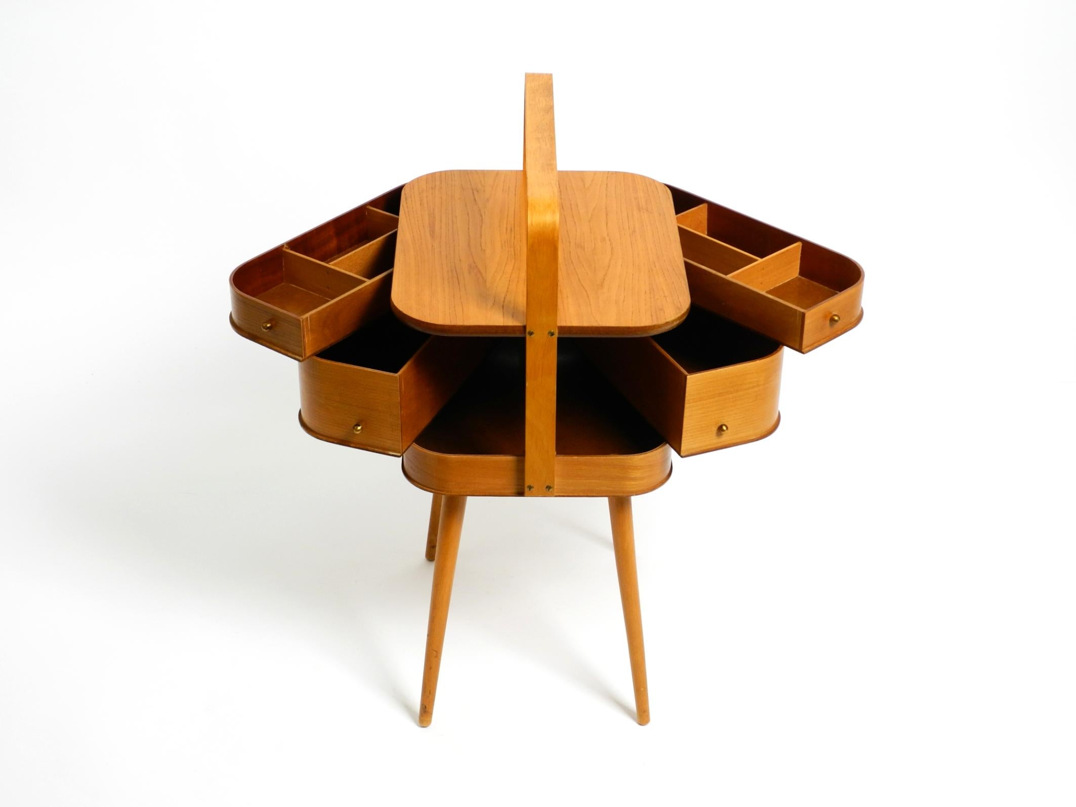 Original Mid Century Modern folding sewing box in very good vintage condition.
The entire box is made of plywood with teak veneer. Buttons for opening are made of brass.
A fantastically beautiful 1950s design with lots of details and storage