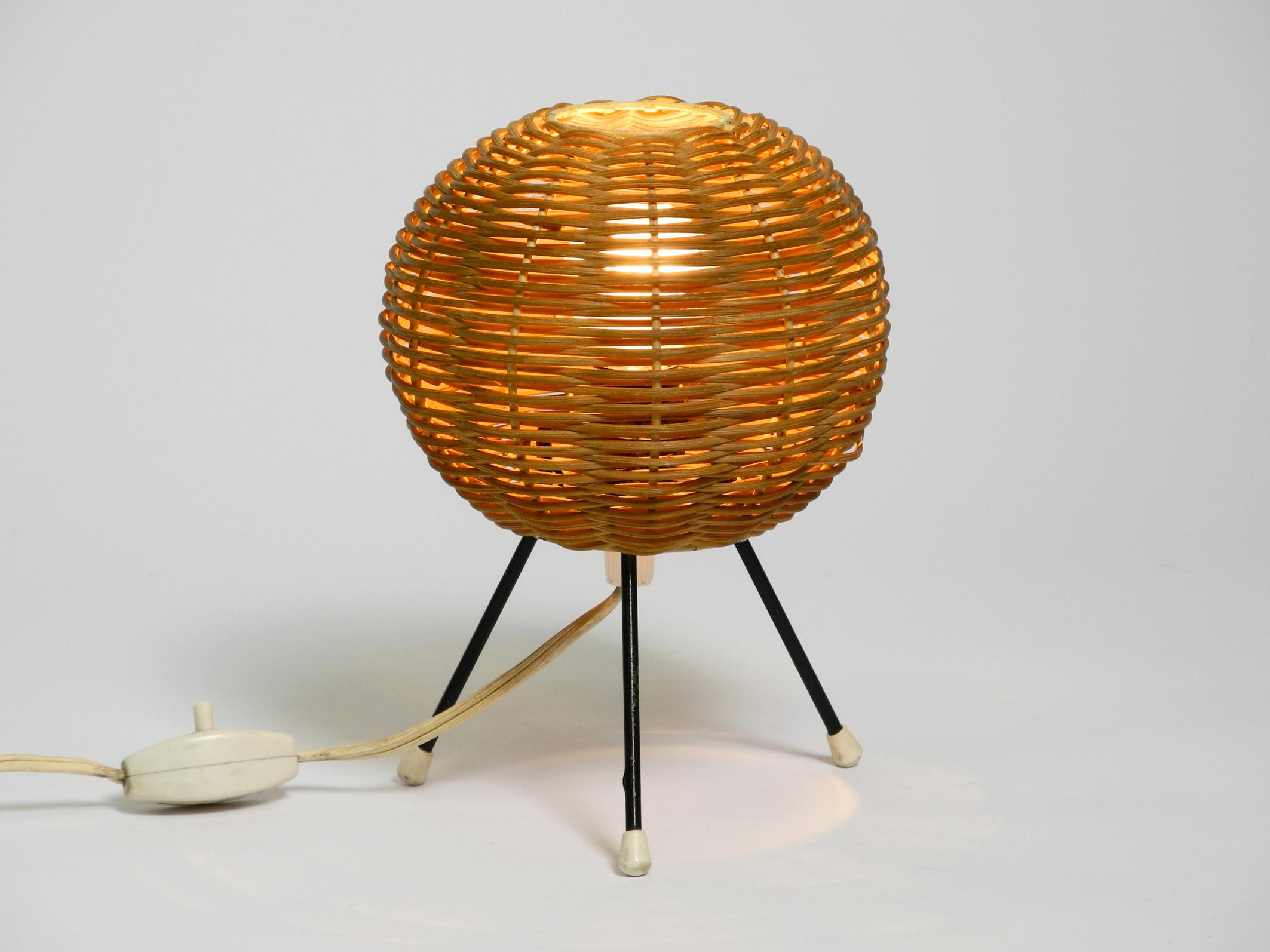 Beautiful original 1950s metal tripod table lamp with wicker lampshade.
Great 50s design in very good vintage condition.
Ball lampshade made of real wicker with a white metal frame.
Black painted metal legs with all three plastic ends.
Great, very