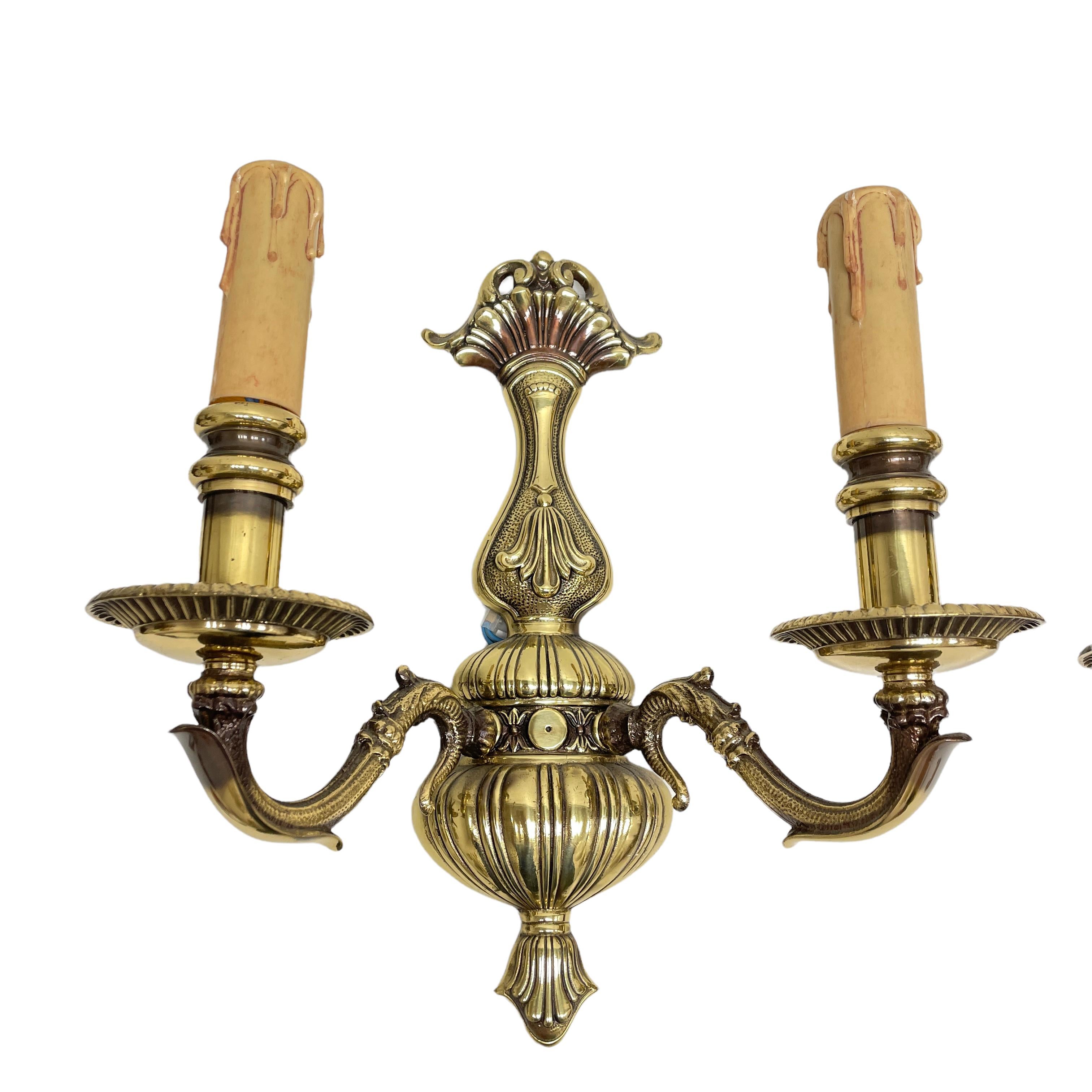 A stunning pair of heavy brass wall sconces. Each consisting of a stylish Hollywood Regency style design. Each fixture requires two European E14 / 110 Volt candelabra bulbs, each bulb up to 40 watts. A nice addition to any room.