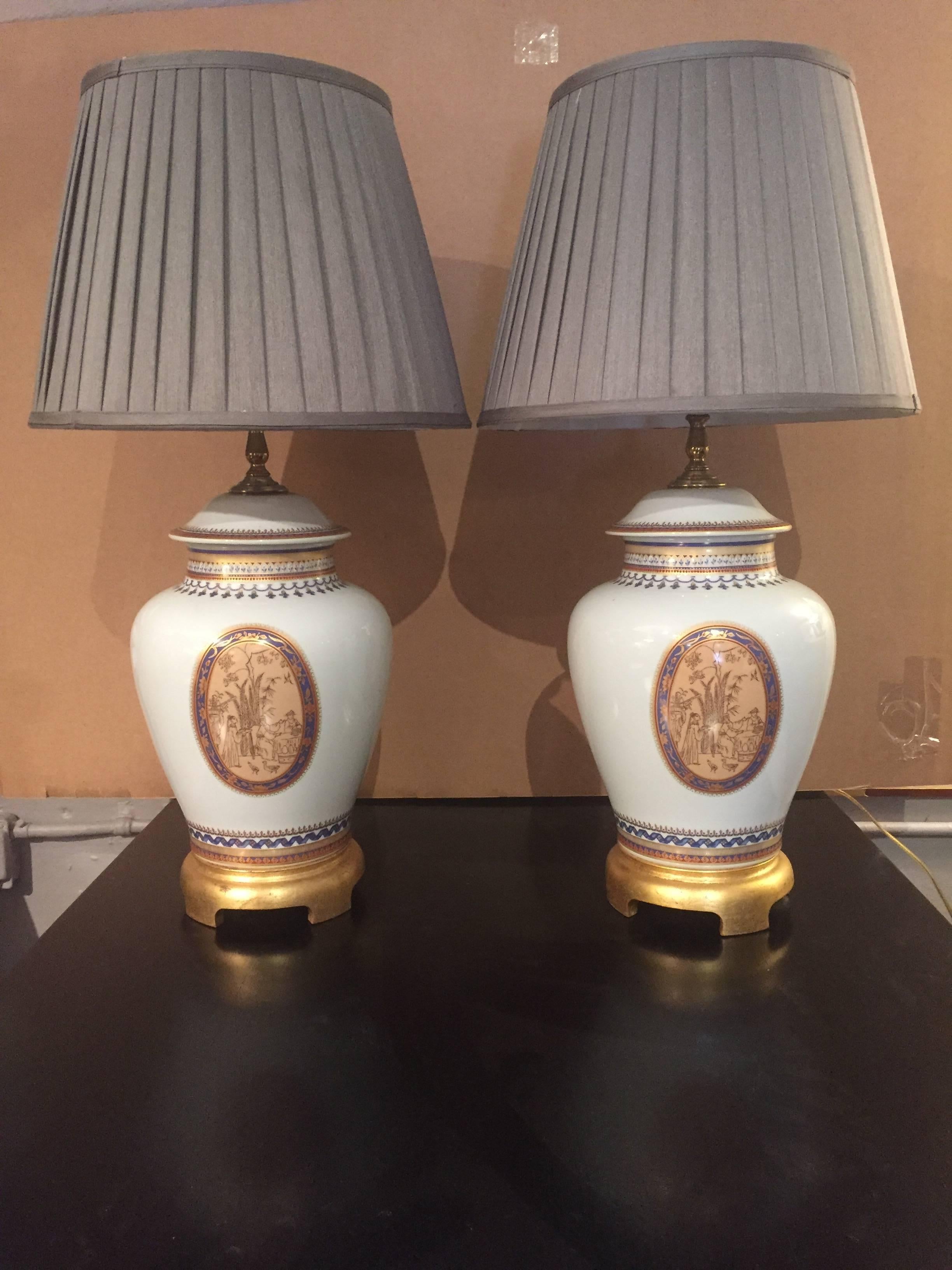 Two ginger jar shaped white porcelain regal table lamps having blue and gold decoration with oval medallions and gilded bases. Custom shades.
Height to socket 22