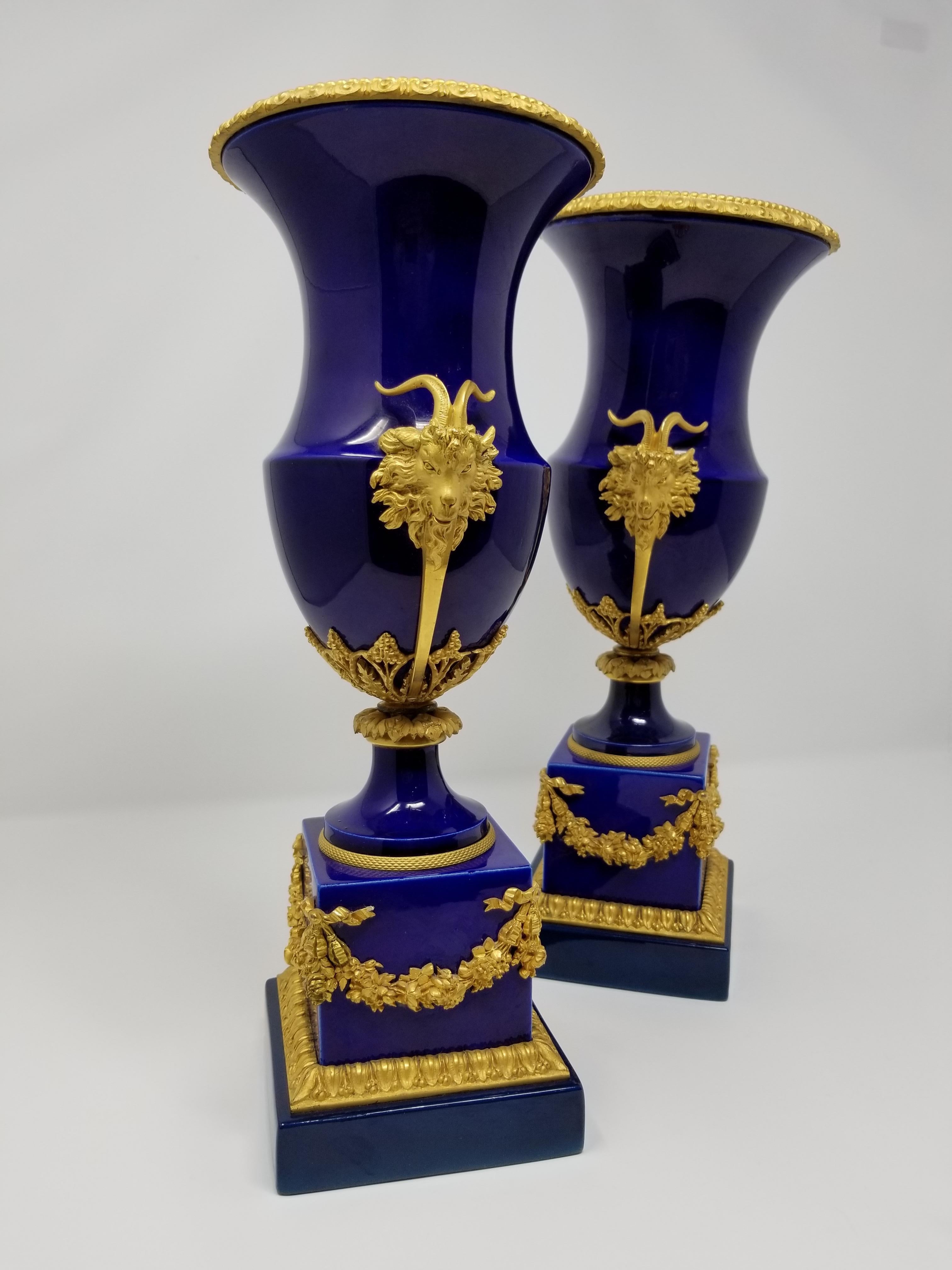 A beautiful pair of 19th century French Louis XVI style Sevres cobalt blue and ormolu-mounted vases with rams heads and wreaths. The porcelain body is beautifully painted with the signature Sevres Royal cobalt blue. The square shaped base is
