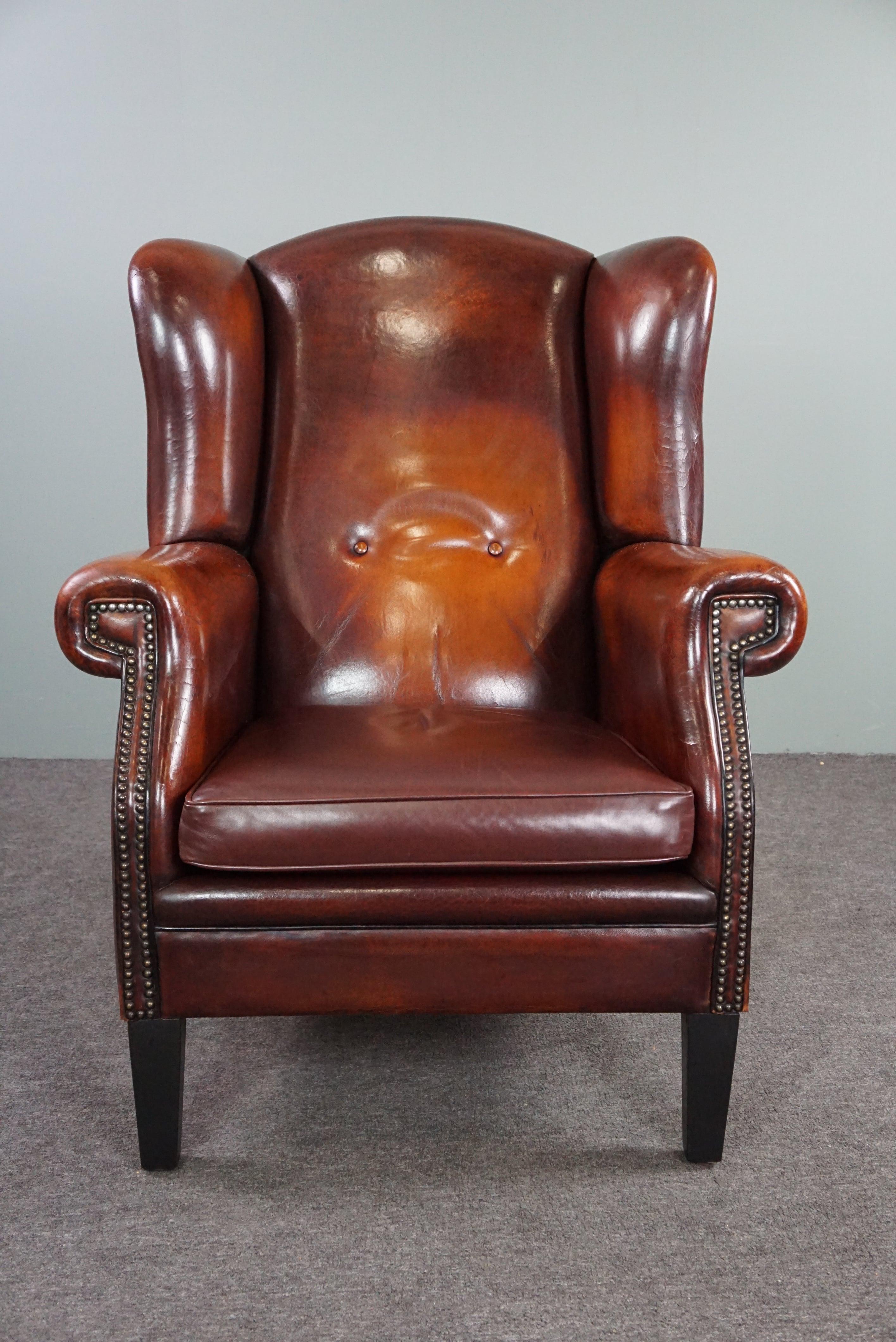 Offered is this beautiful, well-fitting sheepskin leather wing chair.
This sheep leather wing chair has a beautiful deep and warm color, an expressive patina, a comfortable seat, beautiful finish with decorative nails and stands on slender, sleek