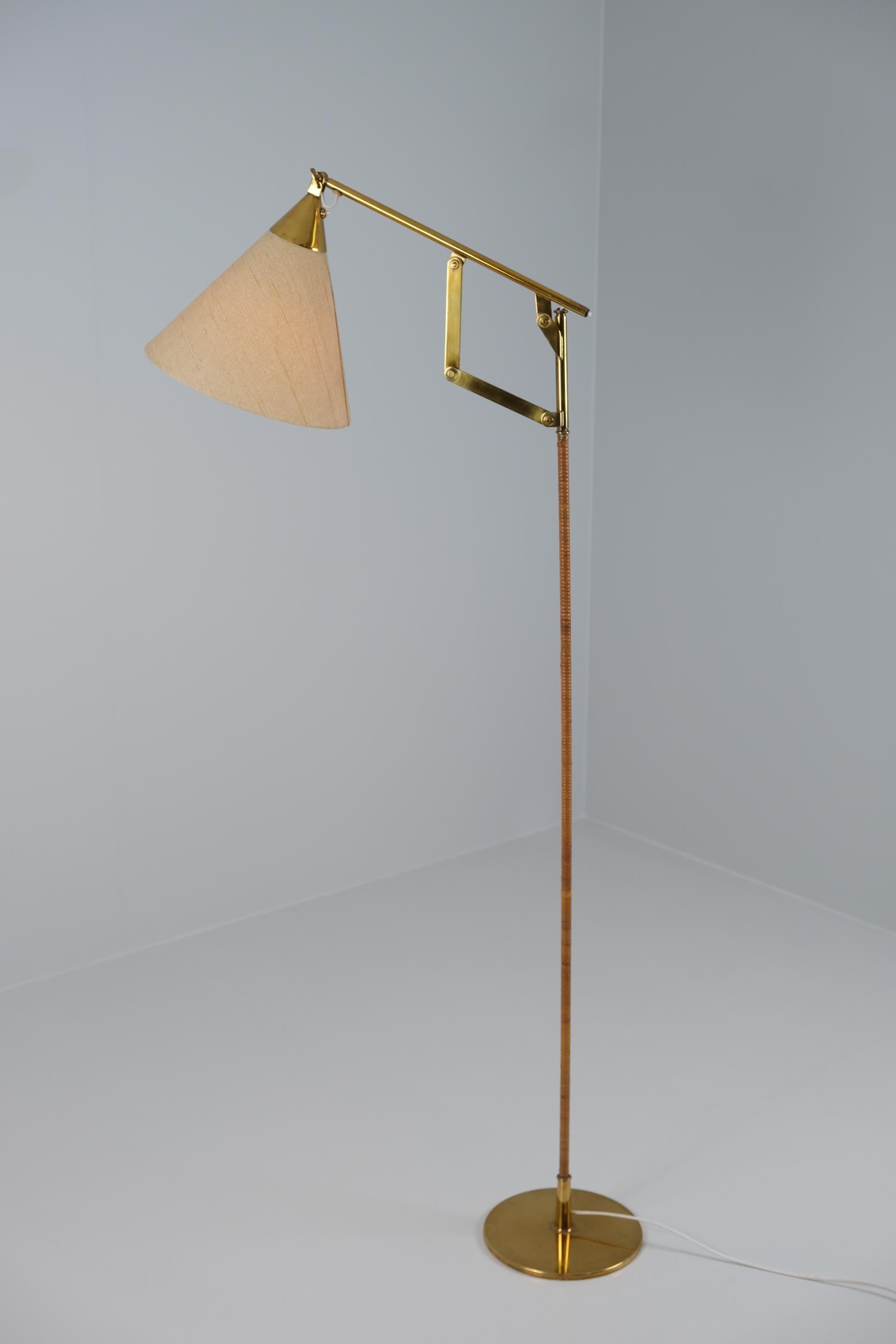 A brass floor lamp model 9605 designed by Paavo Tynell and manufactured by Taito Oy in Finland in the 1950s. This is one of the rarest Paavo Tynell floor lamps, for it is not seen often. Featuring the usual rattan stem, and an adjustable mechanism