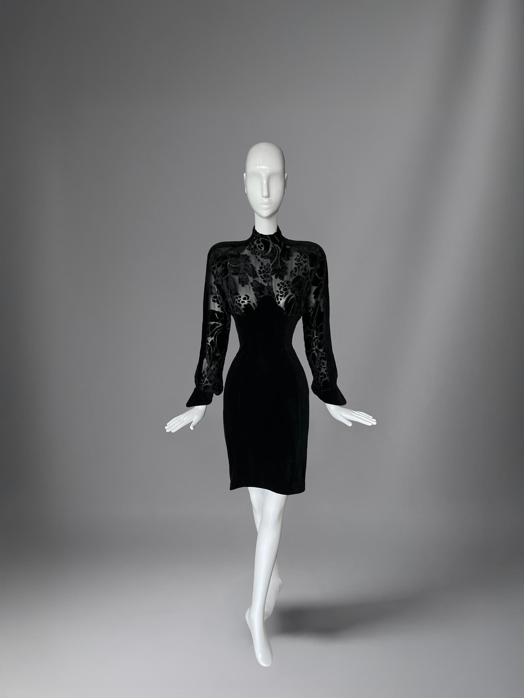 Manfred Thierry Mugler a distillé le drame du velours de minuit et l'intrigue de la peau nue dans cette robe de cocktail dévorée, d'une rareté inouïe : une pièce qui ressemble moins à un vêtement qu'à une mise en scène.
Coupée juste au-dessus du