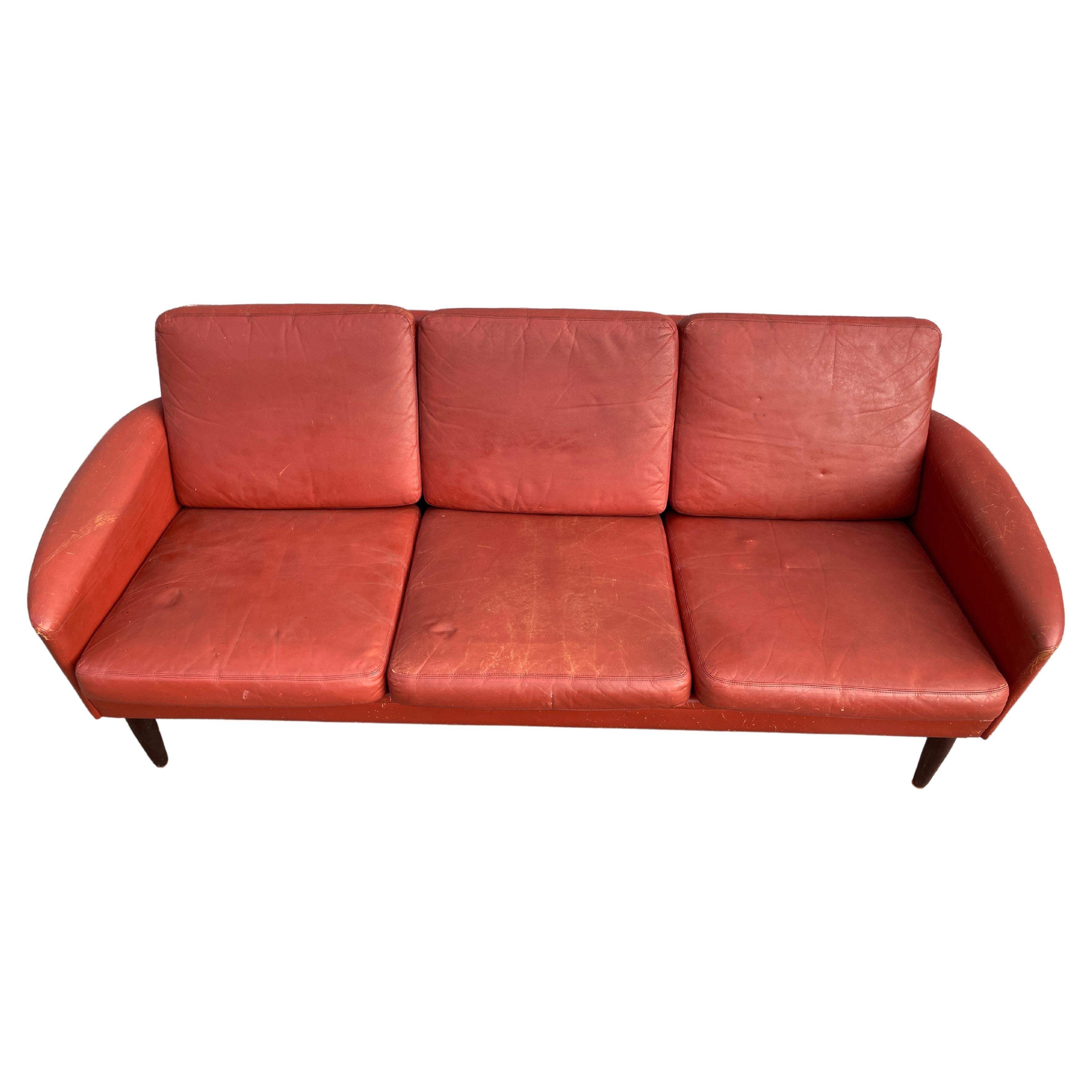 Worn red Leather low 6 foot smaller low 3-seat Danish modern sofa with rosewood legs. Style of Designer Hans Olsen. Amazing patina to original rust red color leather. Original leather worn in with scrapes to corners scuffs marks and cracks all