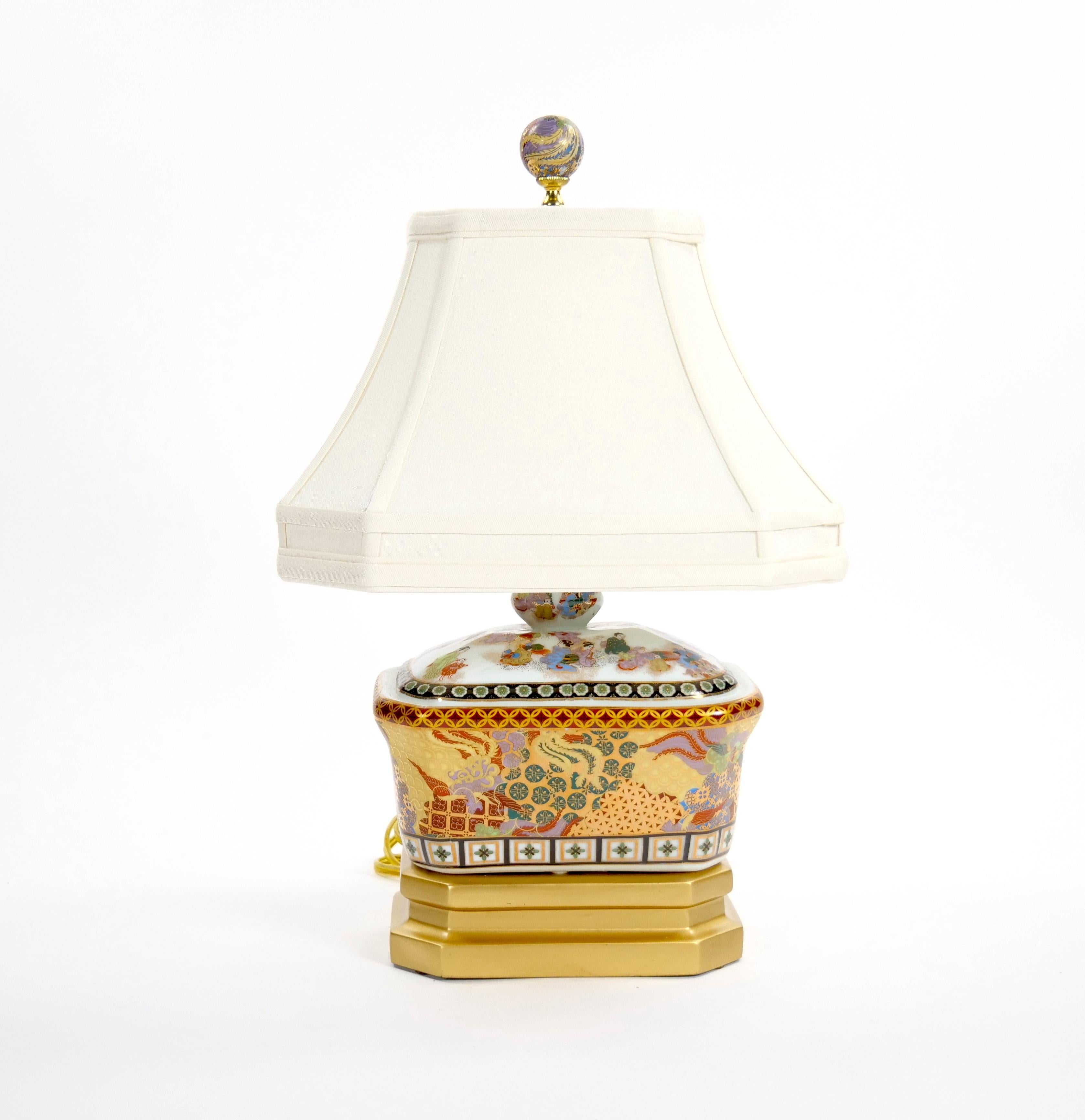 Diese exquisite Porzellan-Tischlampe aus dem 20. Jahrhundert ist ein Beispiel für außergewöhnliche Handwerkskunst mit wunderschön gemalten Dekorationen im Satsuma-Stil und eleganten vergoldeten Details. Der rechteckige, vasenförmige Lampenkörper ist