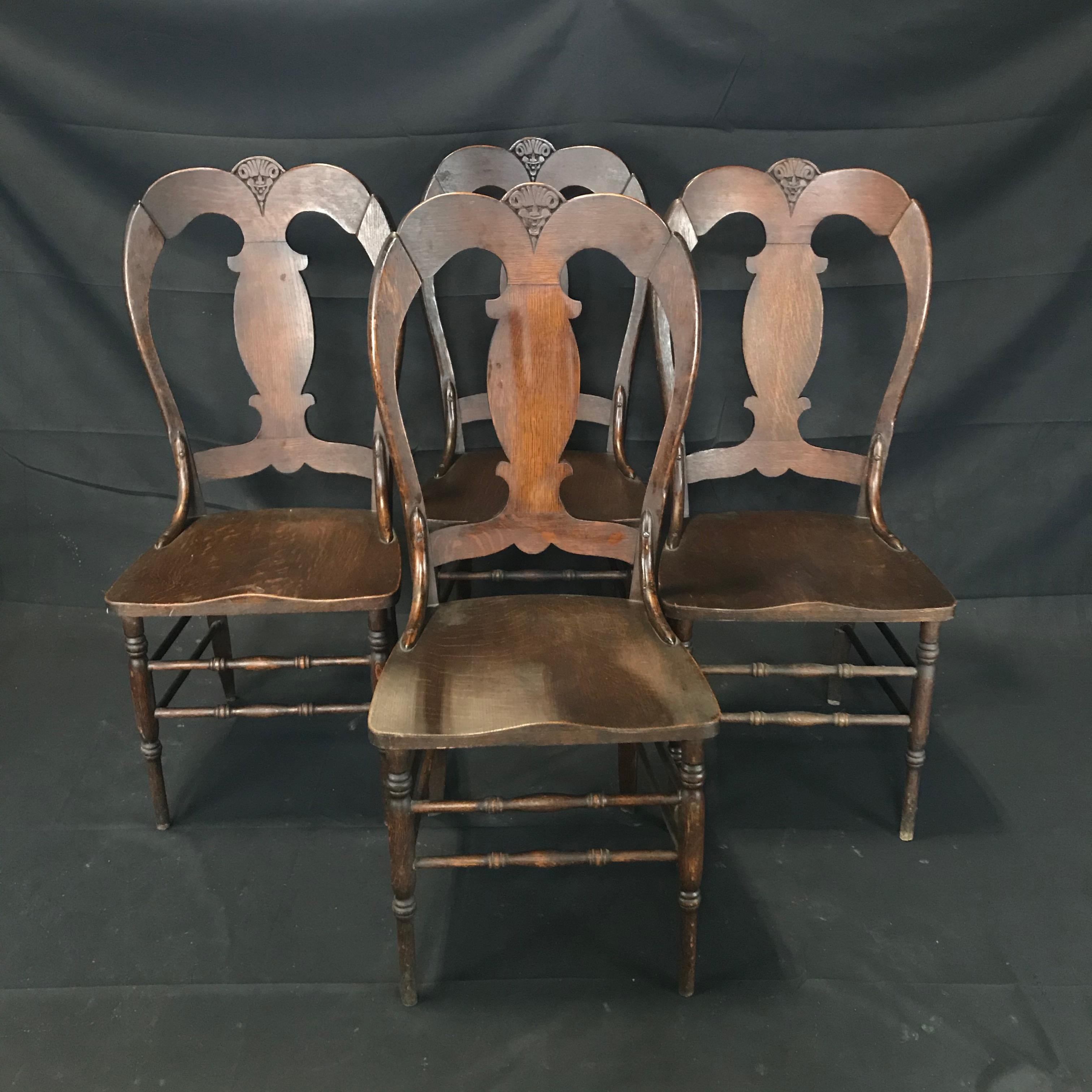 A whimsically carved late 19th century set of four Renaissance Arts and Crafts style figural oak dining chairs featuring a carved face, solid wood construction, beautiful wood grain, and great style and form. New updated contemporary seat cushions