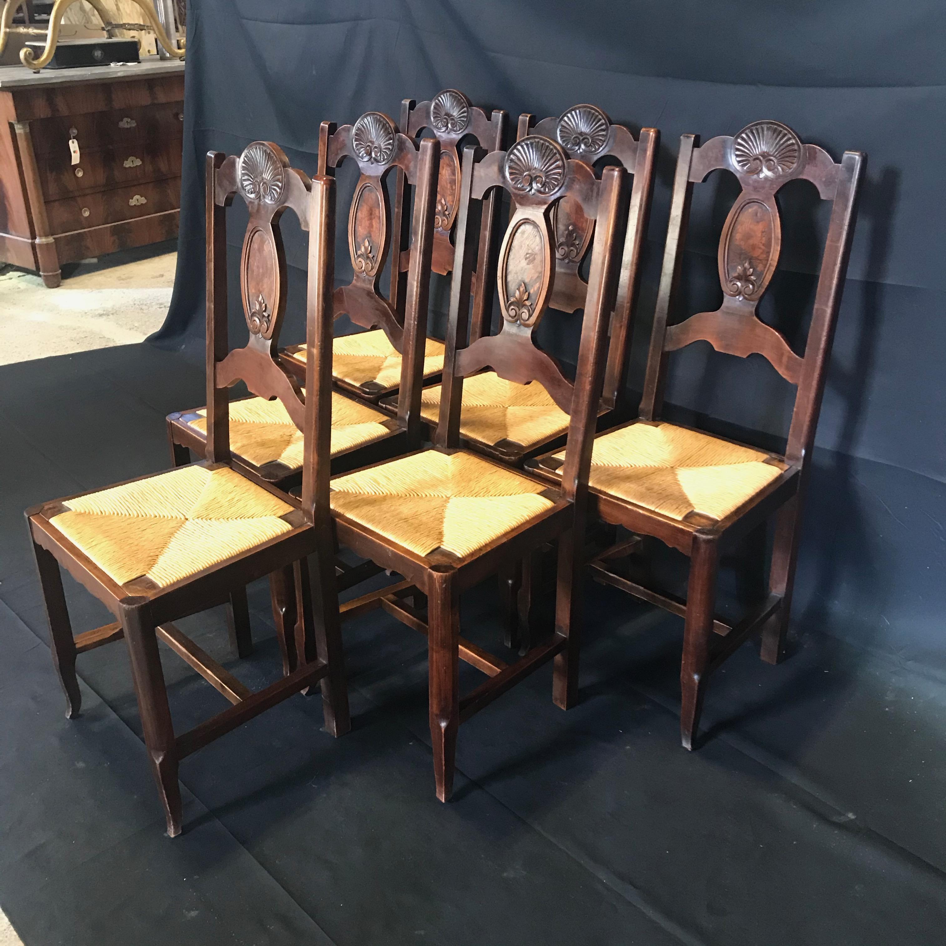 Stunning set of six antique Arts & Crafts or French Country Provincial carved walnut dining chairs with rush seats, all in good condition. Stunning carved shell over an inset burled wood panel, with carved acanthus leaf beneath on back splat.