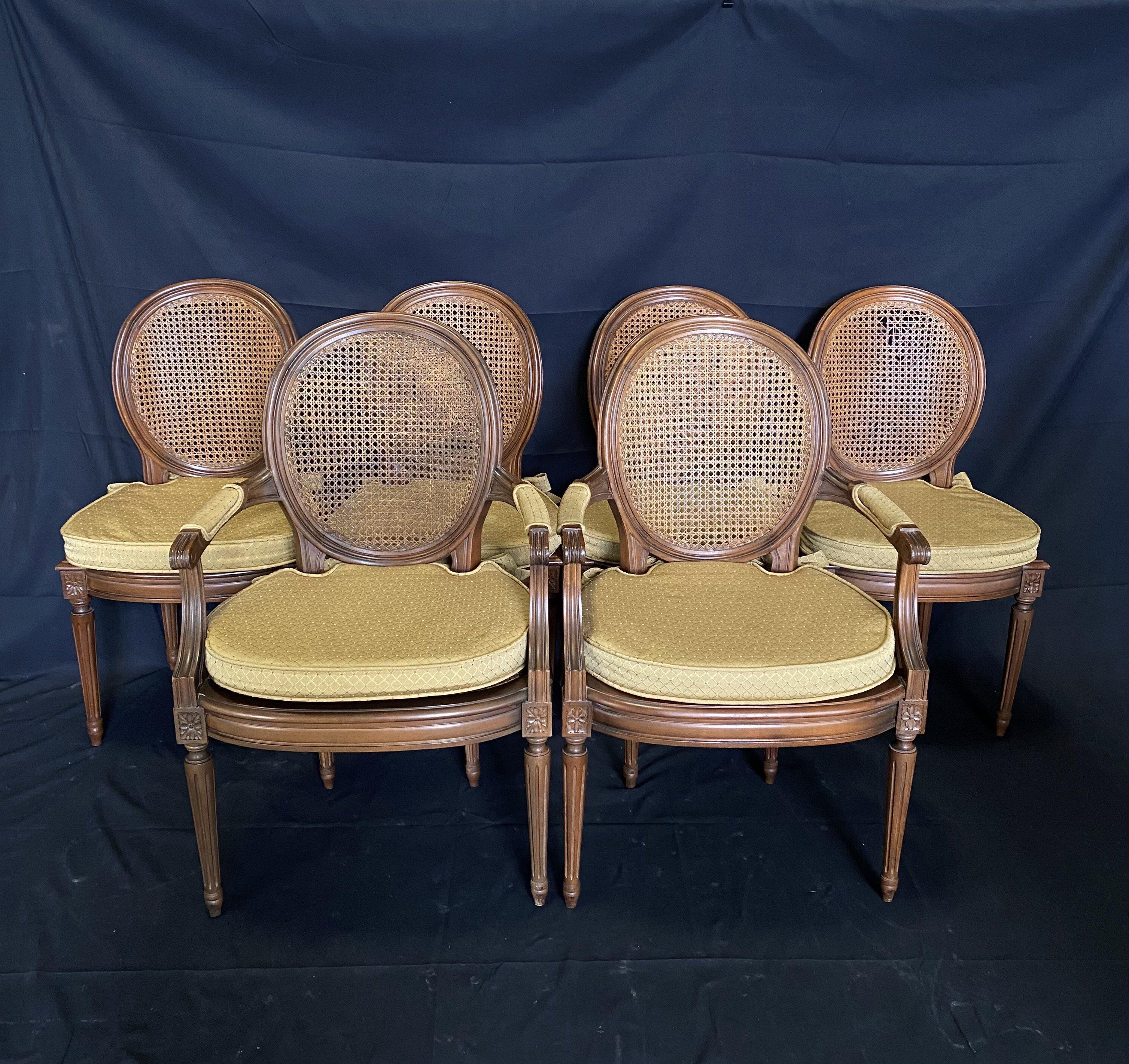 A lovely set of six French Louis XVI style chairs, comprised of four side and two arm chairs. Lovely original caning complemented with neutral seat cushions. Reeded tapered legs and carved floral embellishments on top. Entire chair is carved with