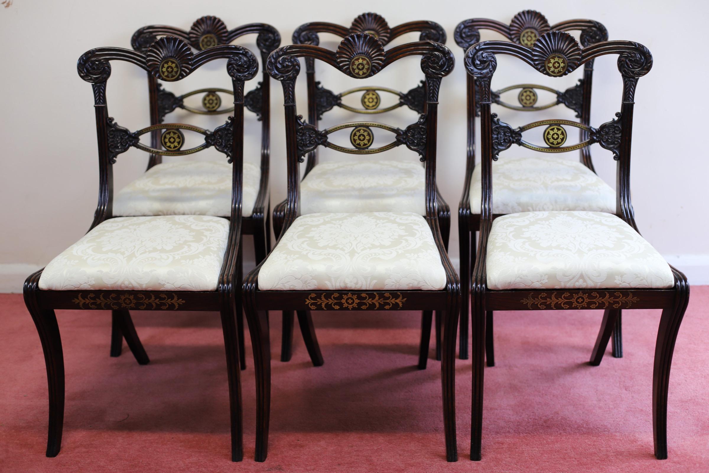 We delight to offer for sale this fantastic Set of Six Regency hardwood and Brass-Inlaid Dining Chairs, early 19th century, recovered in cream silk damask, the acanthus-scrolled and reeded top rails centred by a shell, a brass-inlaid horizontal
