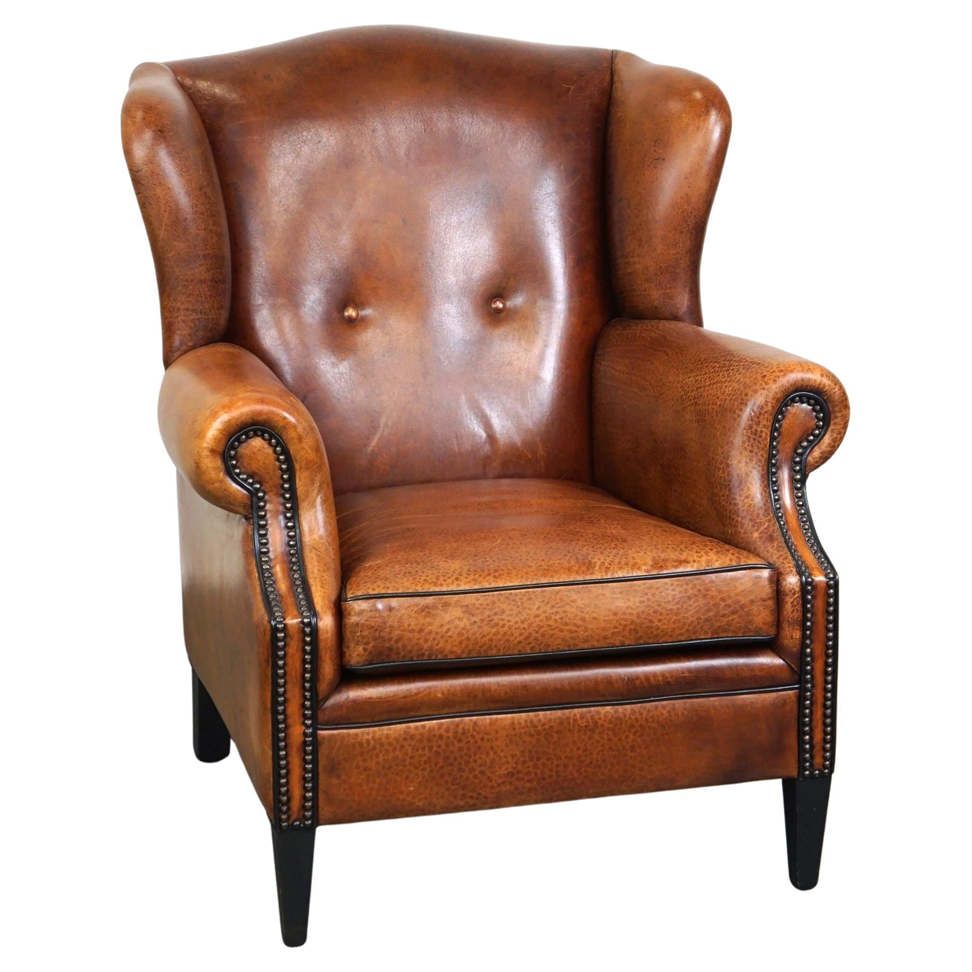 Precioso sillón orejero de piel de oveja, con clavos y ribetes negros