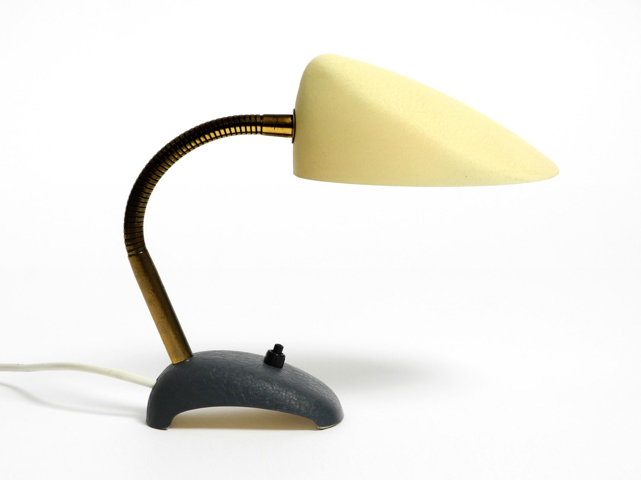 Beautiful small 1950s metal table lamp with brass gooseneck.
Manufacturer is Gebrüder Cosack. Made in Germany.
Mustard yellow shrink varnish on the shade and grey-blue base.
Shell-shaped lampshade, steplessly adjustable to all sides. Holds in any