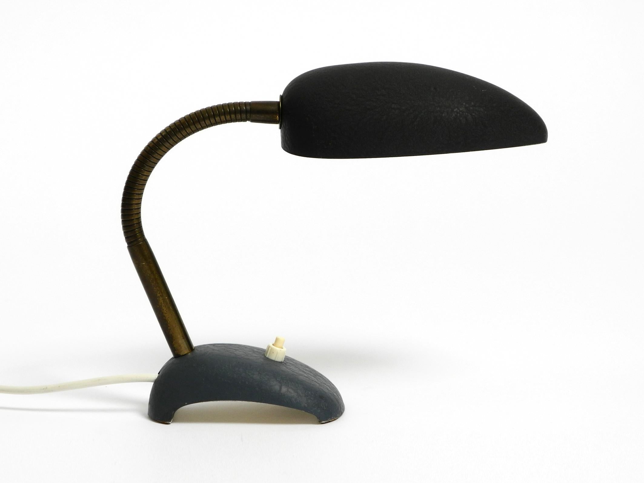Beautiful small 1950s metal table lamp with brass gooseneck.
Manufacturer is Gebrüder Cosack. Made in Germany.
Black shrink varnish on the shade and grey-blue base.
Shell-shaped lampshade, steplessly adjustable to all sides. Holds in any