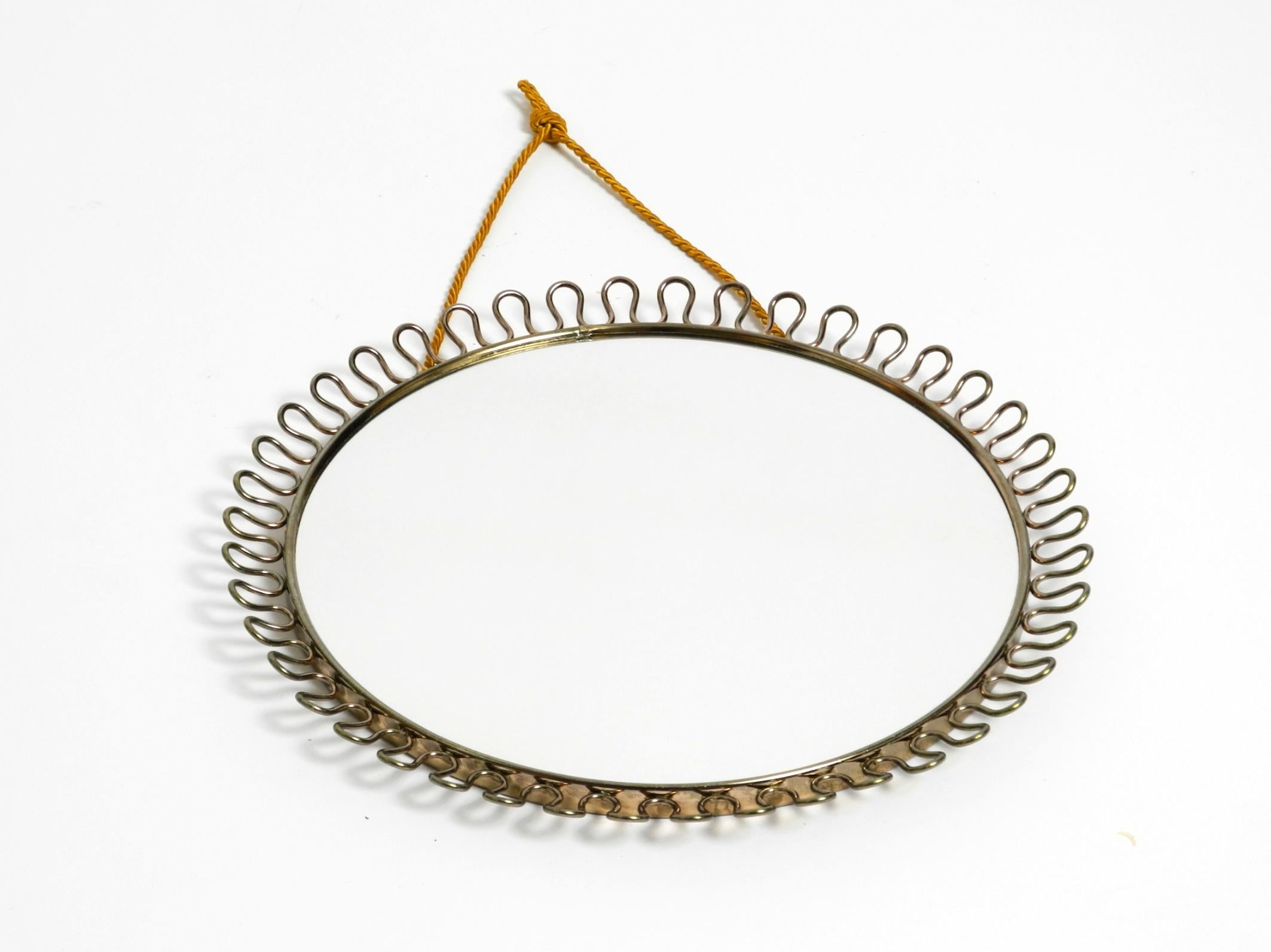 Bellissimo piccolo specchio da parete in metallo originale del Mid Century.
La struttura in metallo è di colore ottone e presenta un design ad anello. Ha una corda pendente color oro. Nessun danno all'intero specchio.
Il vetro dello specchio non è