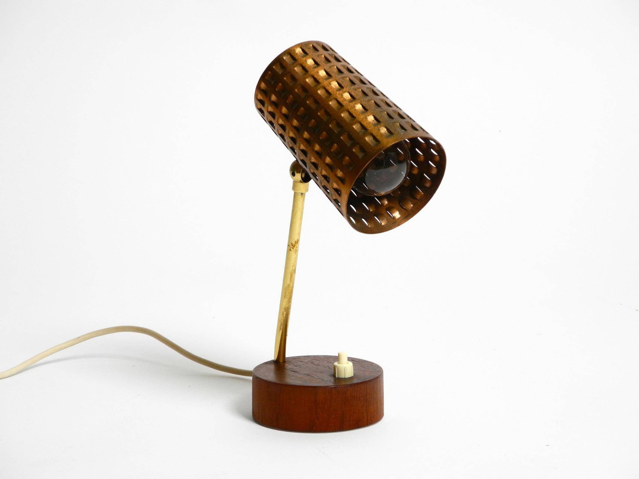 Rare, beautiful Mid Century Modern table lamp with perforated sheet shade made of copper, neck is made of brass. Base is with teak veneer.
Very nice design from the 1950s with great patina.
The shade can be steplessly adjusted up and down and stays