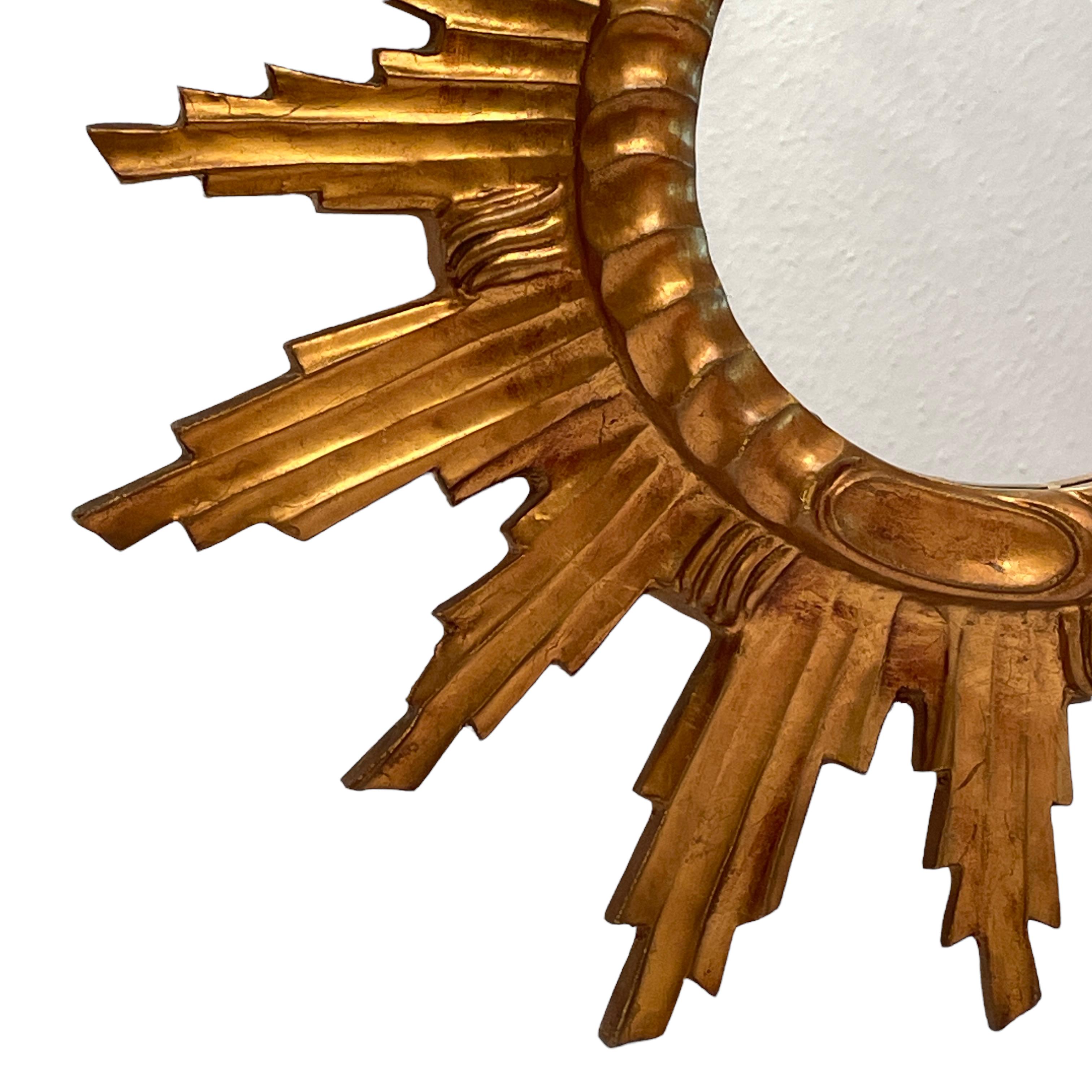 Un beau miroir en forme de starburst. Réalisé en composition dorée et en bois. Il mesure environ 22,13 pouces de diamètre, le miroir lui-même mesure environ 7,38 pouces de diamètre. Il se tient à environ 2